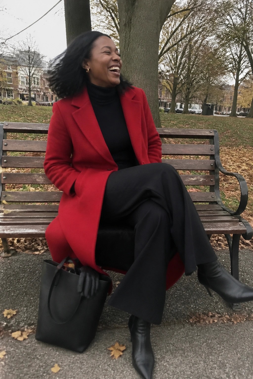 Laughing woman in red coat on park bench with black tote bag nearby