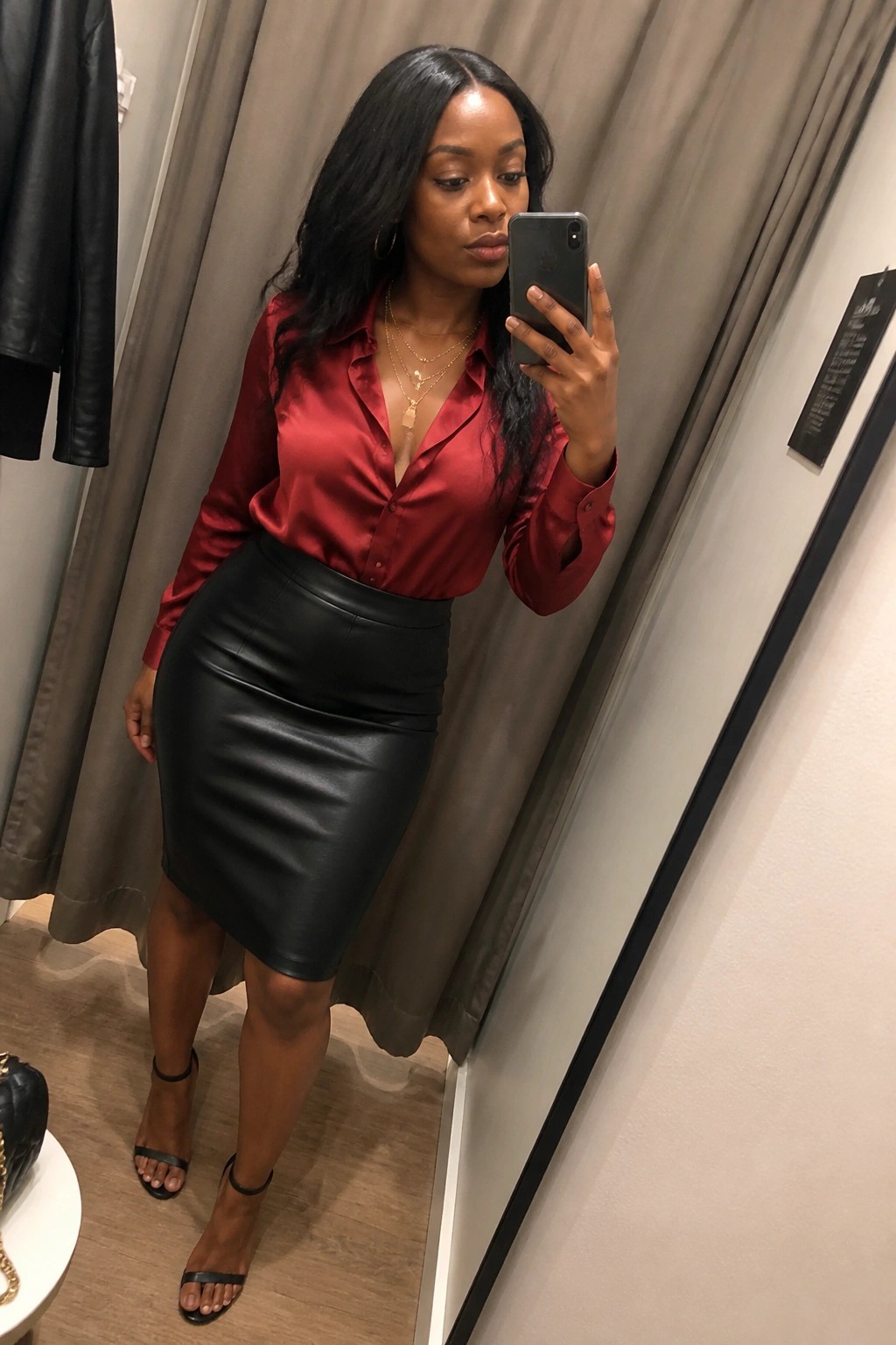 Woman in red satin blouse and black leather skirt taking mirror selfie with phone