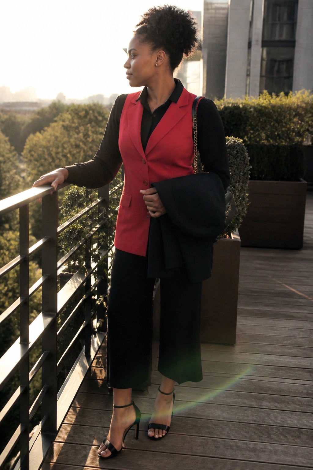 Woman in red vest and black outfit leaning on balcony railing at sunset