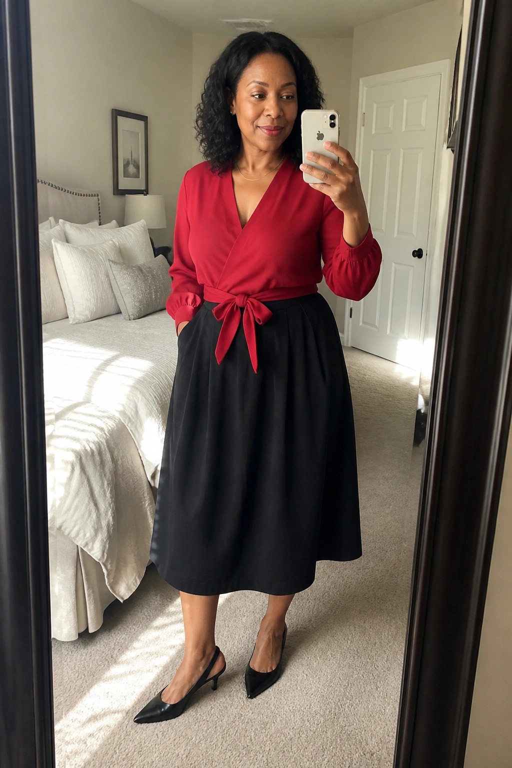 Woman in red wrap blouse and black skirt taking mirror selfie in bedroom
