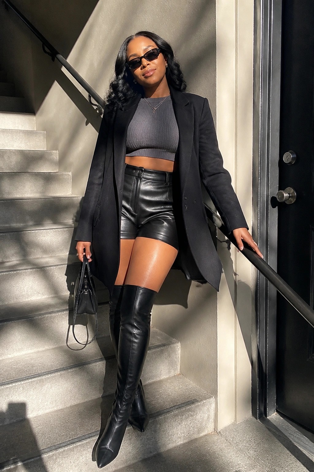 Woman in black blazer, leather shorts, and thigh-high boots on stone stairs.
