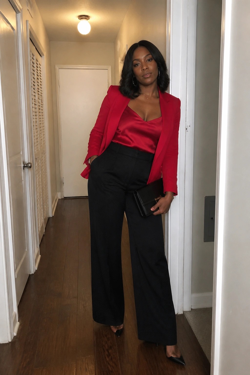 Woman in red blazer over satin top with black wide-leg pants in hallway