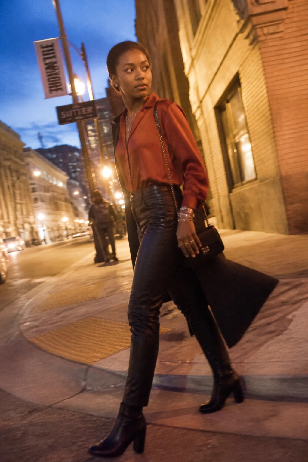 Woman in red satin blouse and black leather pants on city street at dusk
