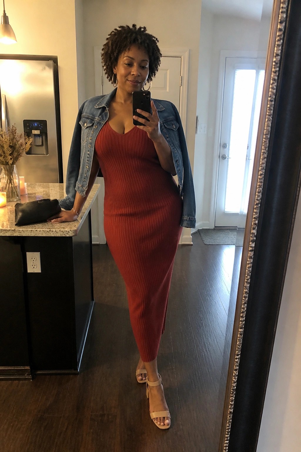 Woman in red ribbed dress and denim jacket taking mirror selfie at home