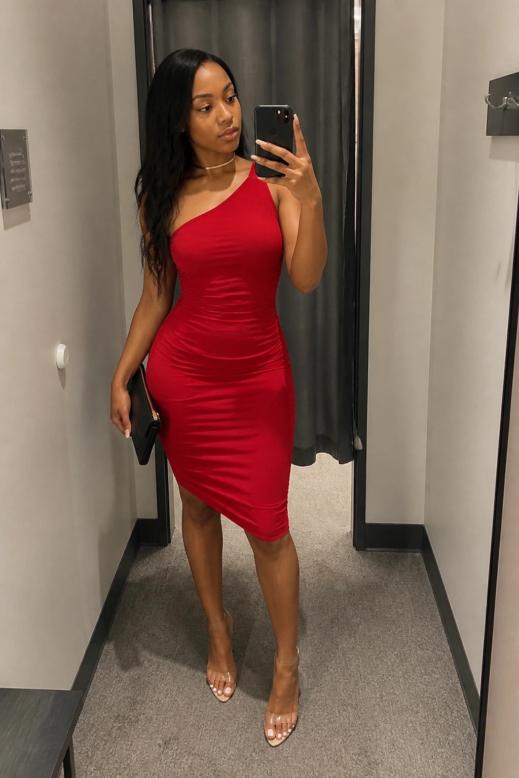 Woman in red one-shoulder dress taking mirror selfie with phone in fitting room