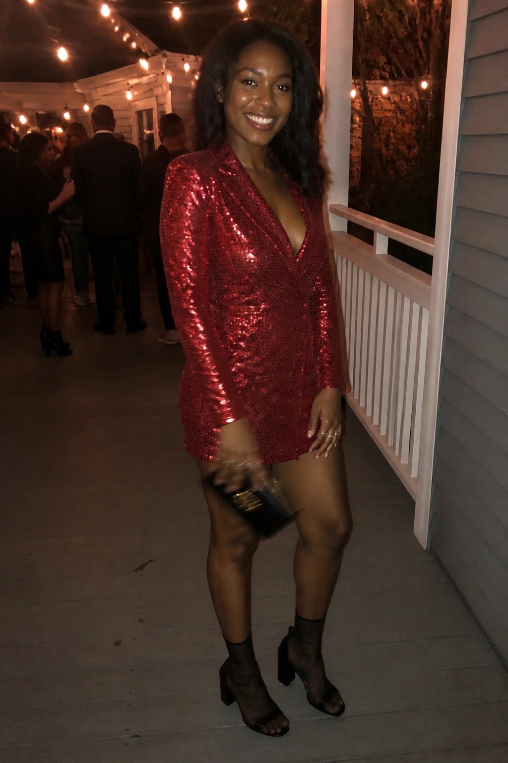 Smiling woman in red sequined mini dress holding clutch at night party