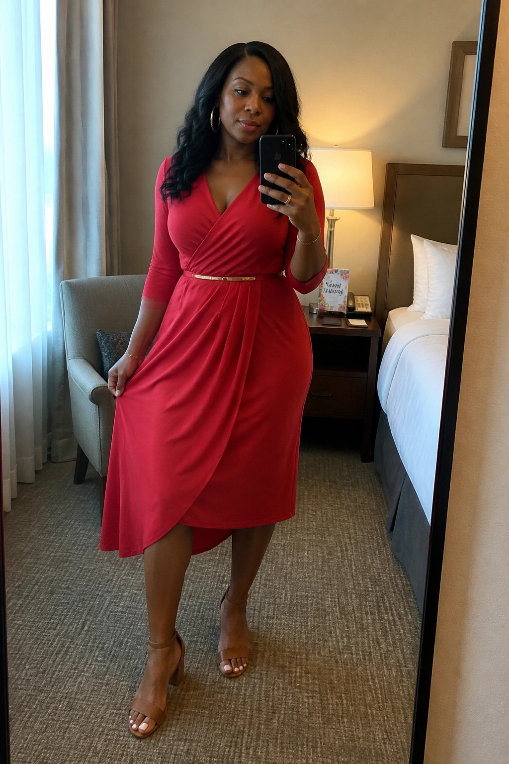 Woman in red wrap dress taking mirror selfie in hotel room with beige decor