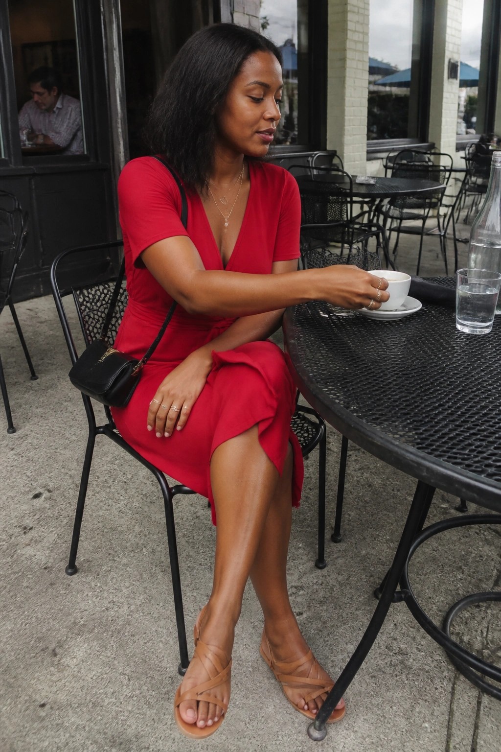Woman in red dress holding coffee at outdoor black metal cafe table