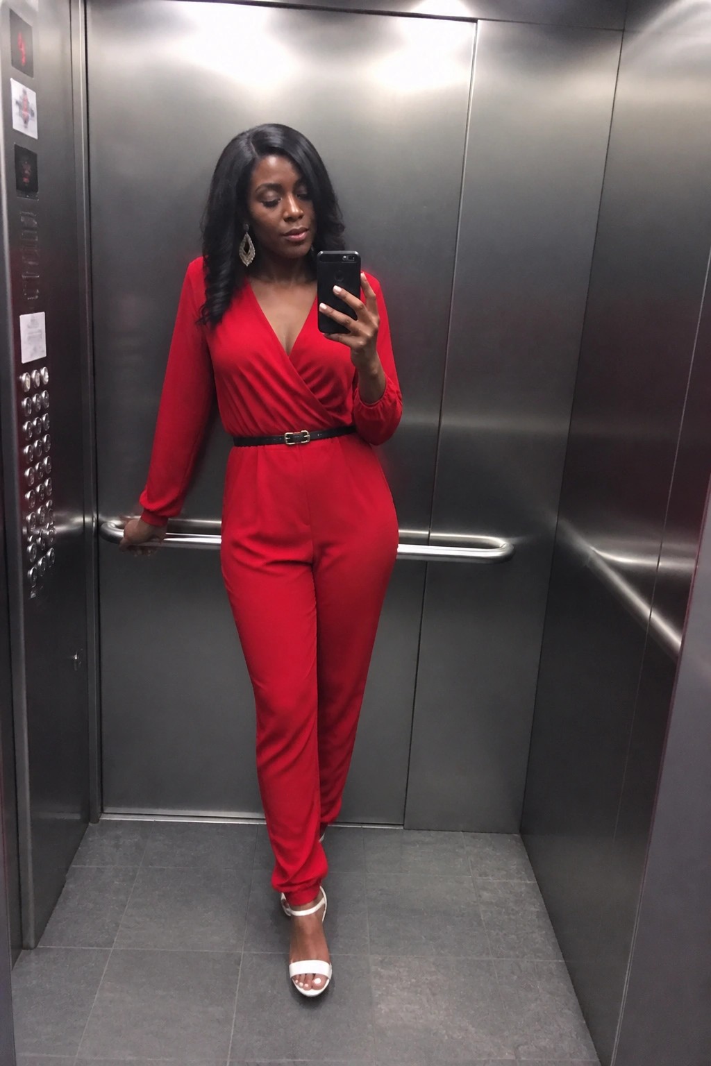 Woman in red jumpsuit taking a selfie inside a metallic elevator