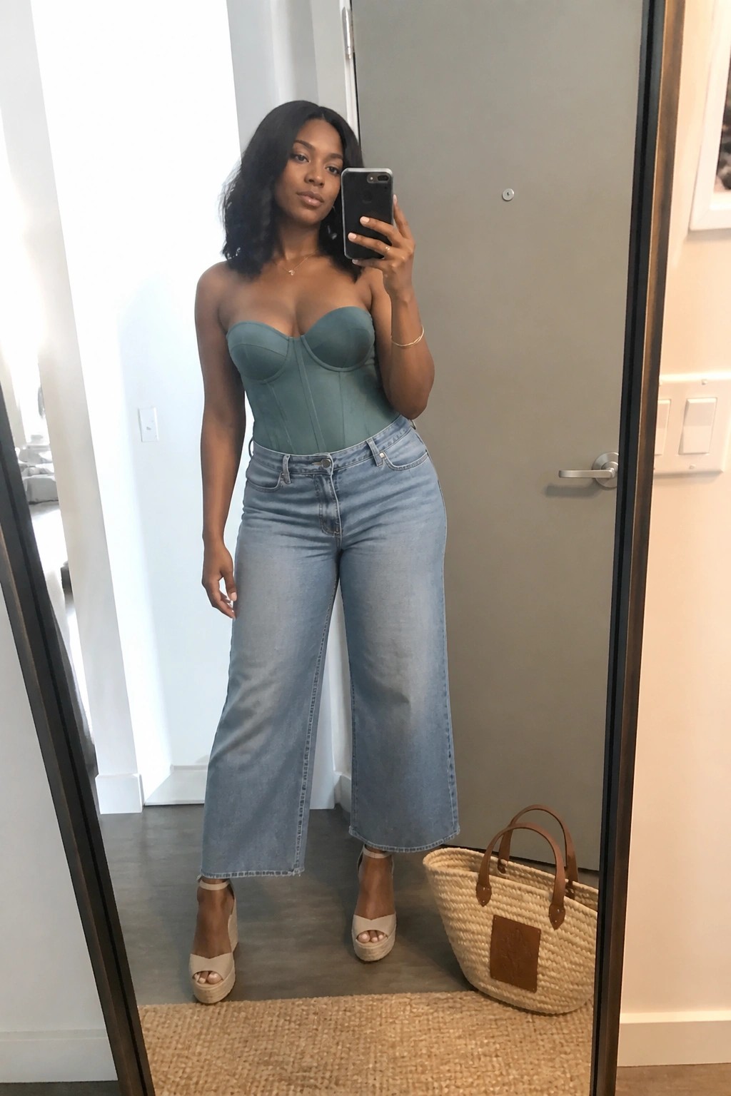 Woman in teal corset and light blue wide-leg jeans taking mirror selfie