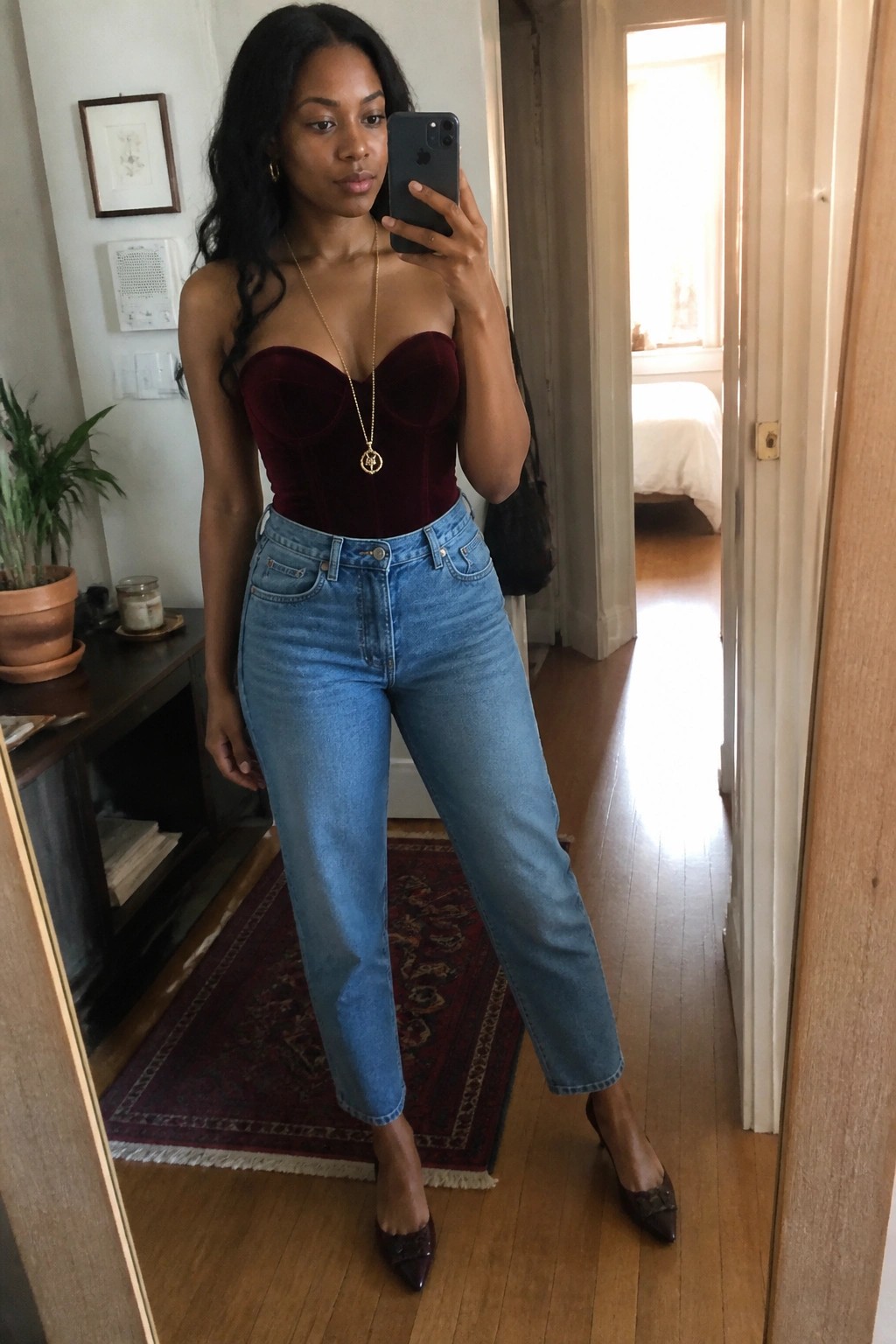 Woman in burgundy velvet corset and blue jeans taking mirror selfie with phone