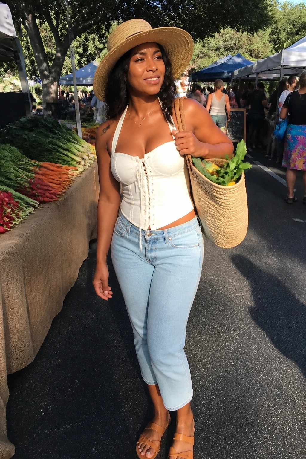 Woman in white corset top, jeans, and straw hat at farmers market with woven bag