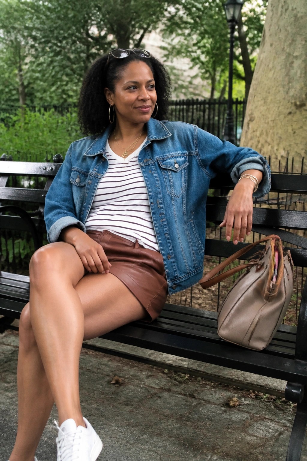 Woman in denim jacket and brown skirt on park bench with handbag