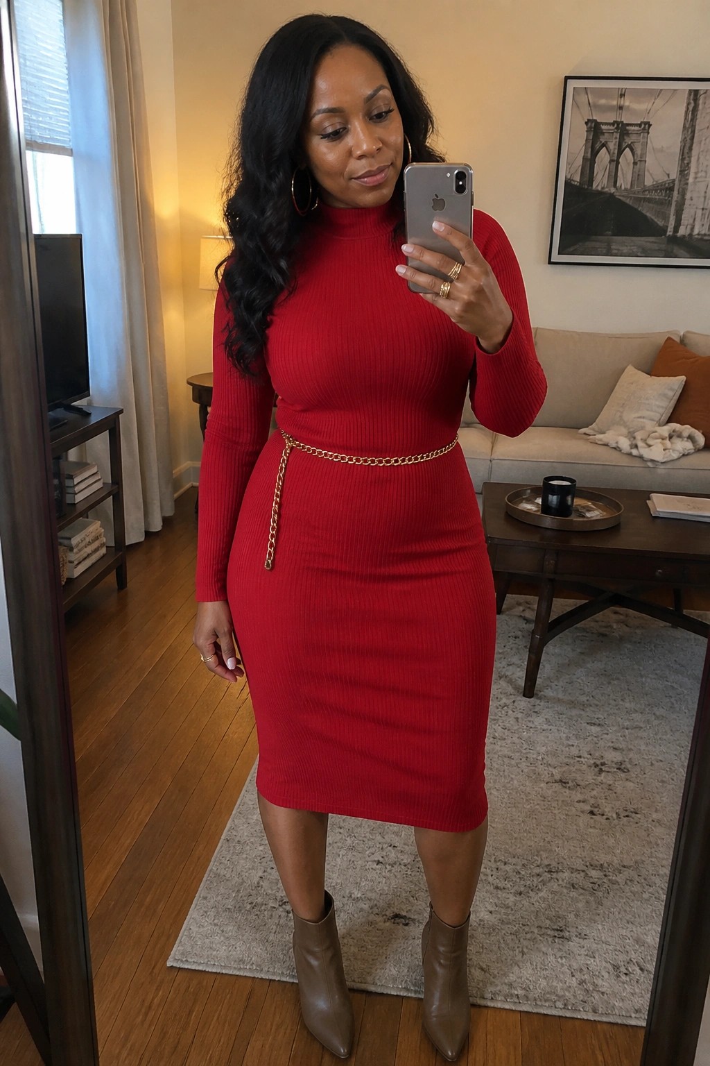 Woman in red ribbed dress with gold chain belt taking mirror selfie in living room