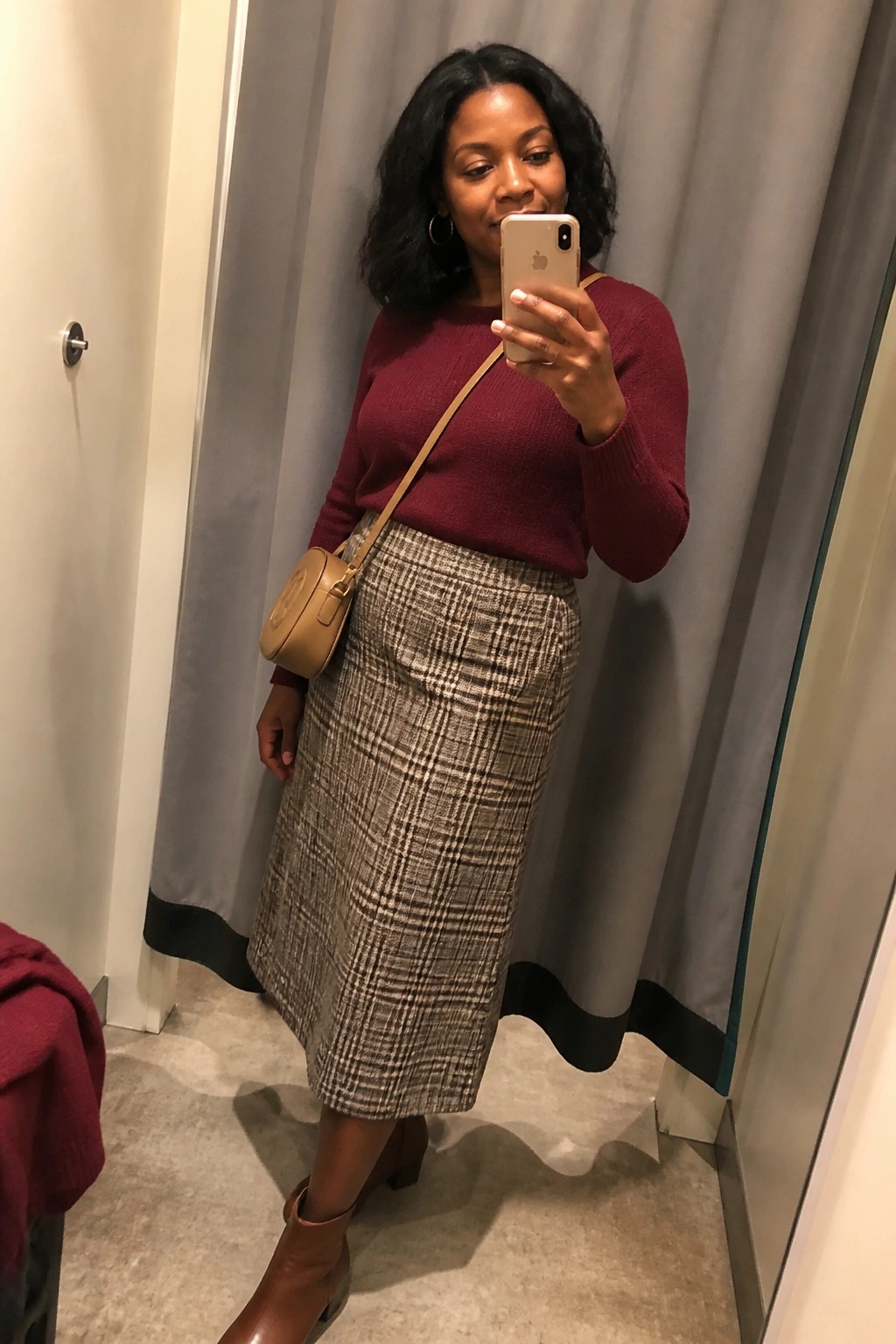 Woman in maroon sweater and plaid skirt taking mirror selfie in fitting room