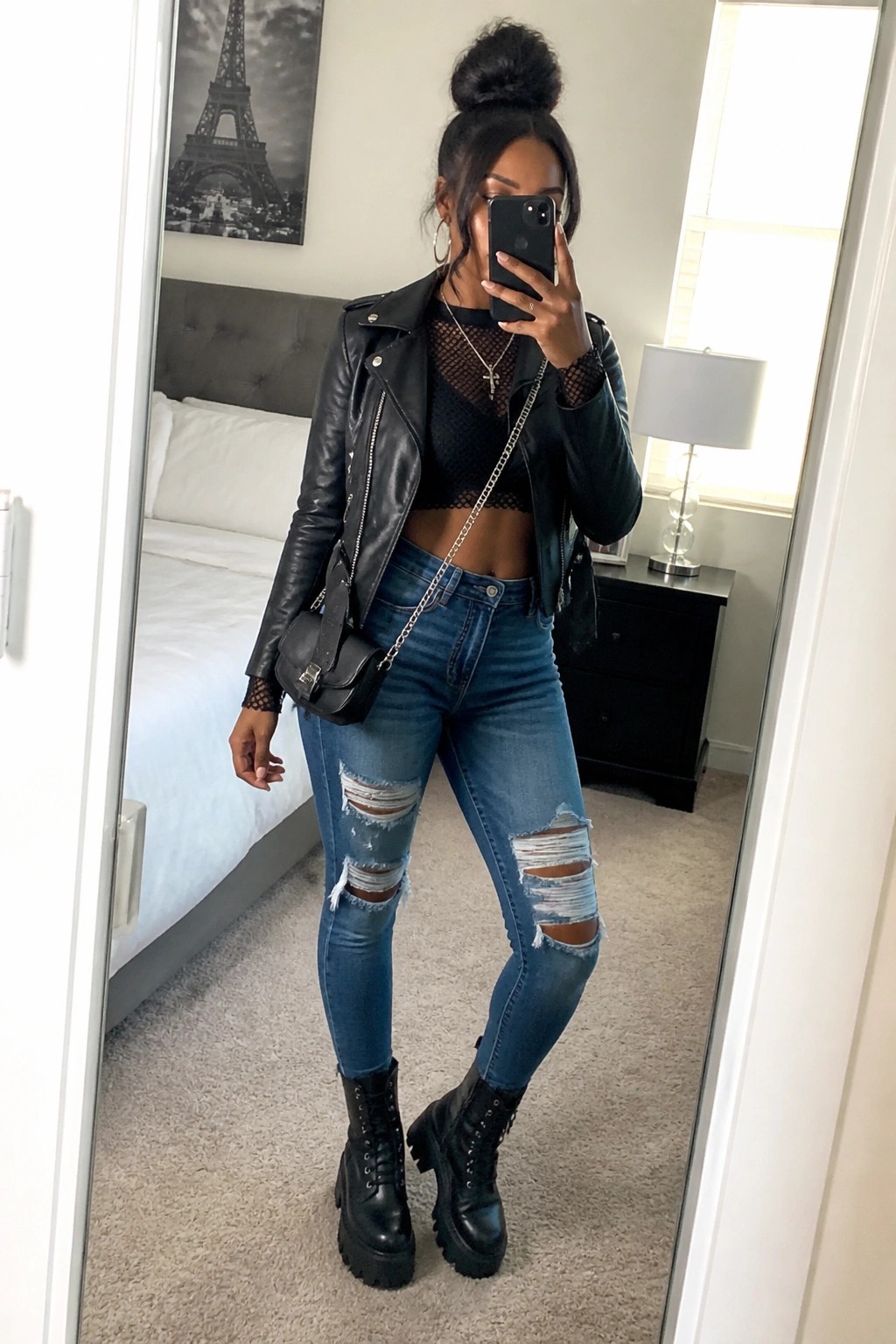 Woman in black leather jacket, mesh top, ripped jeans, and combat boots posing