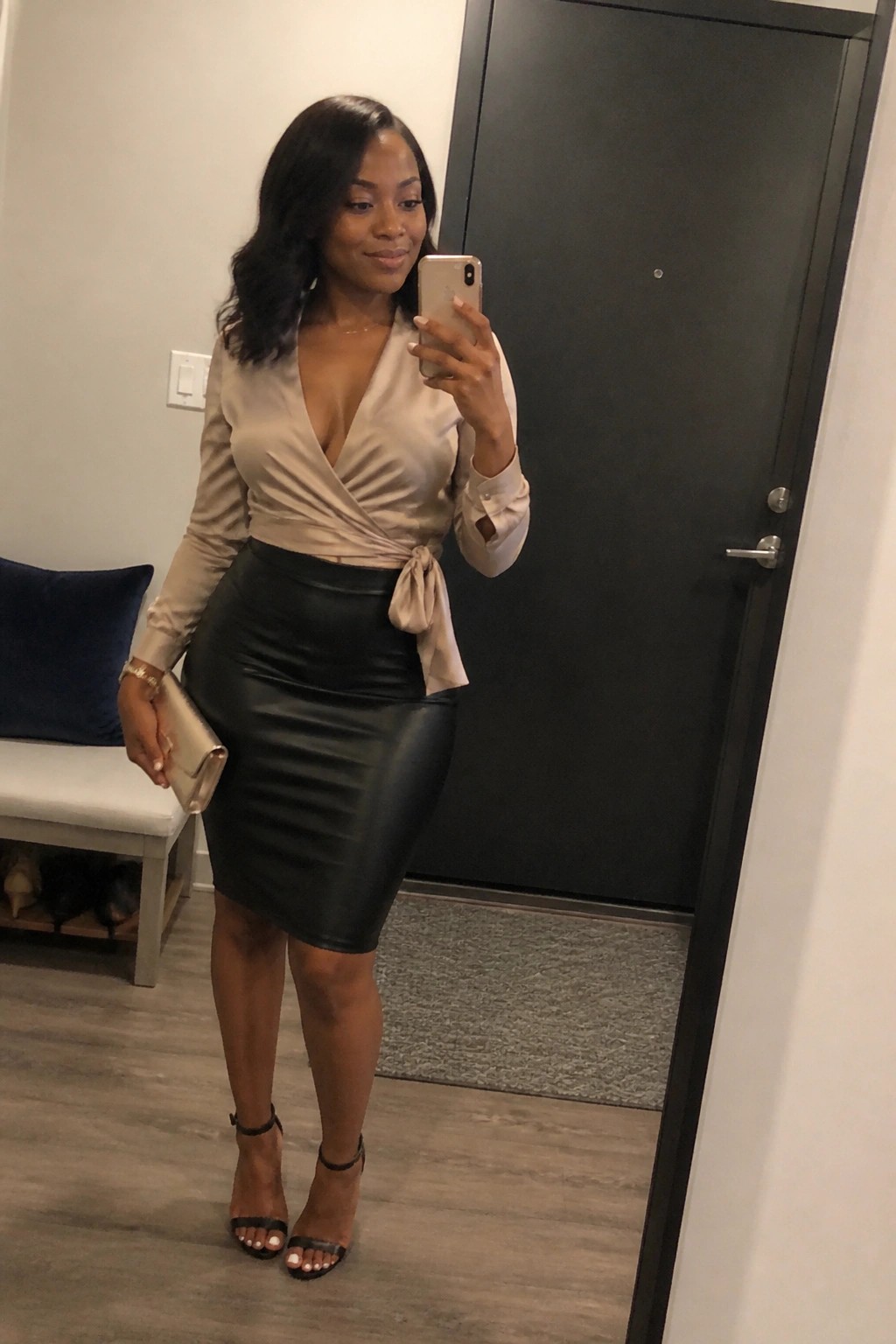 Woman in beige satin wrap blouse and black leather skirt taking mirror selfie