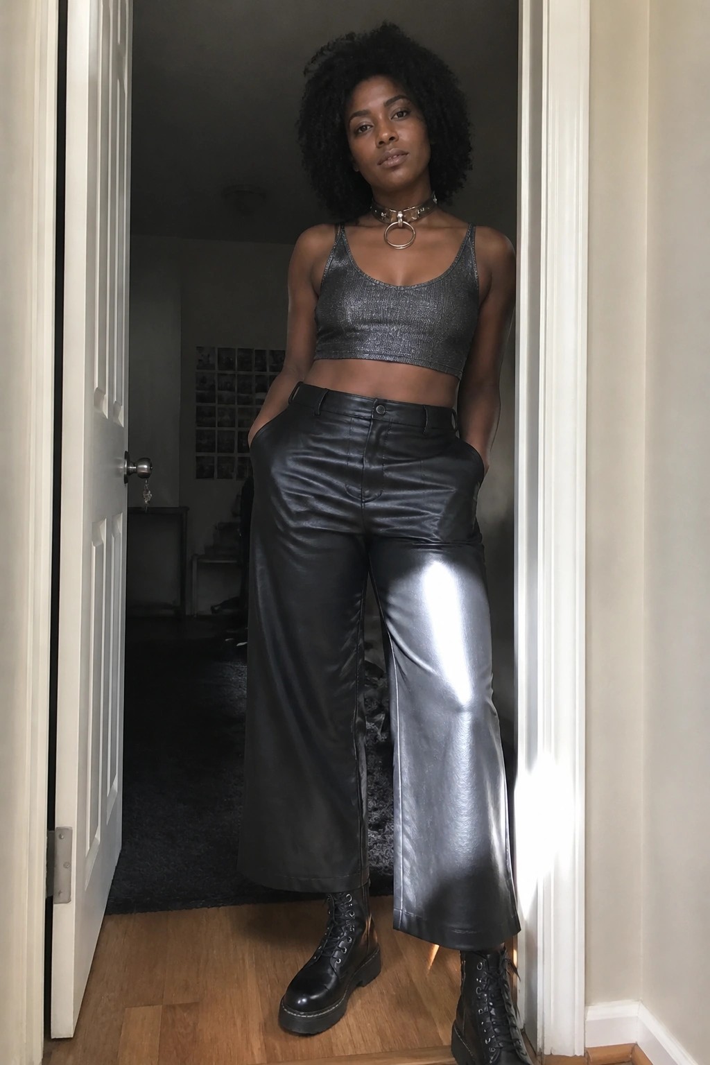Woman with afro hair in silver crop top, black leather pants, and boots in doorway