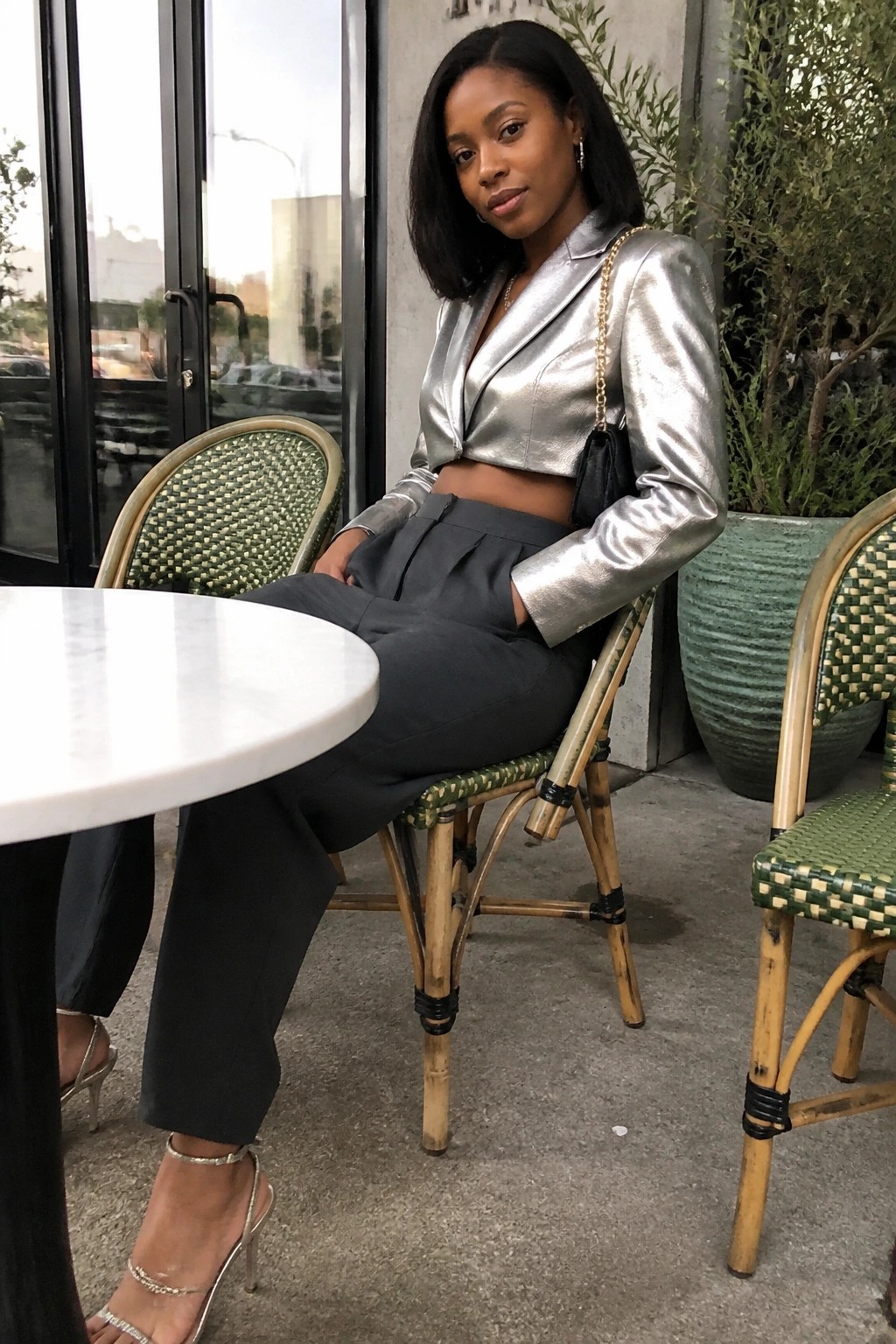 Woman in metallic silver cropped blazer and gray trousers at outdoor cafe table.
