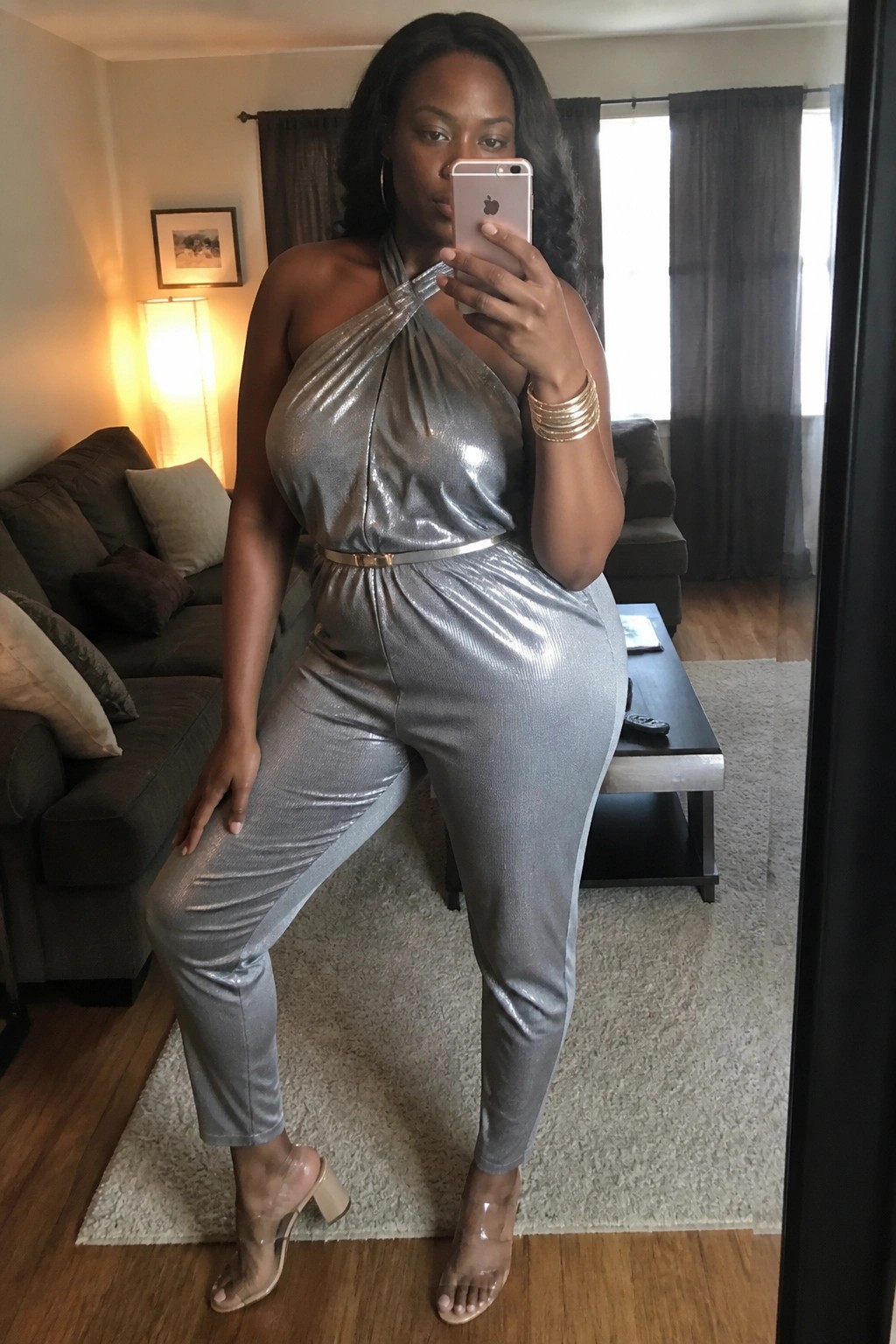 Woman in metallic silver jumpsuit taking mirror selfie in living room