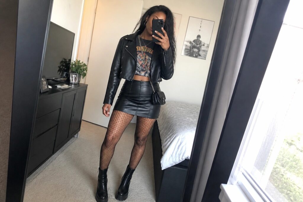 21 Bold Edgy Chic Night Out Outfits for Black Women Woman in black leather jacket, mini skirt, fishnets, and boots taking bedroom mirror selfie