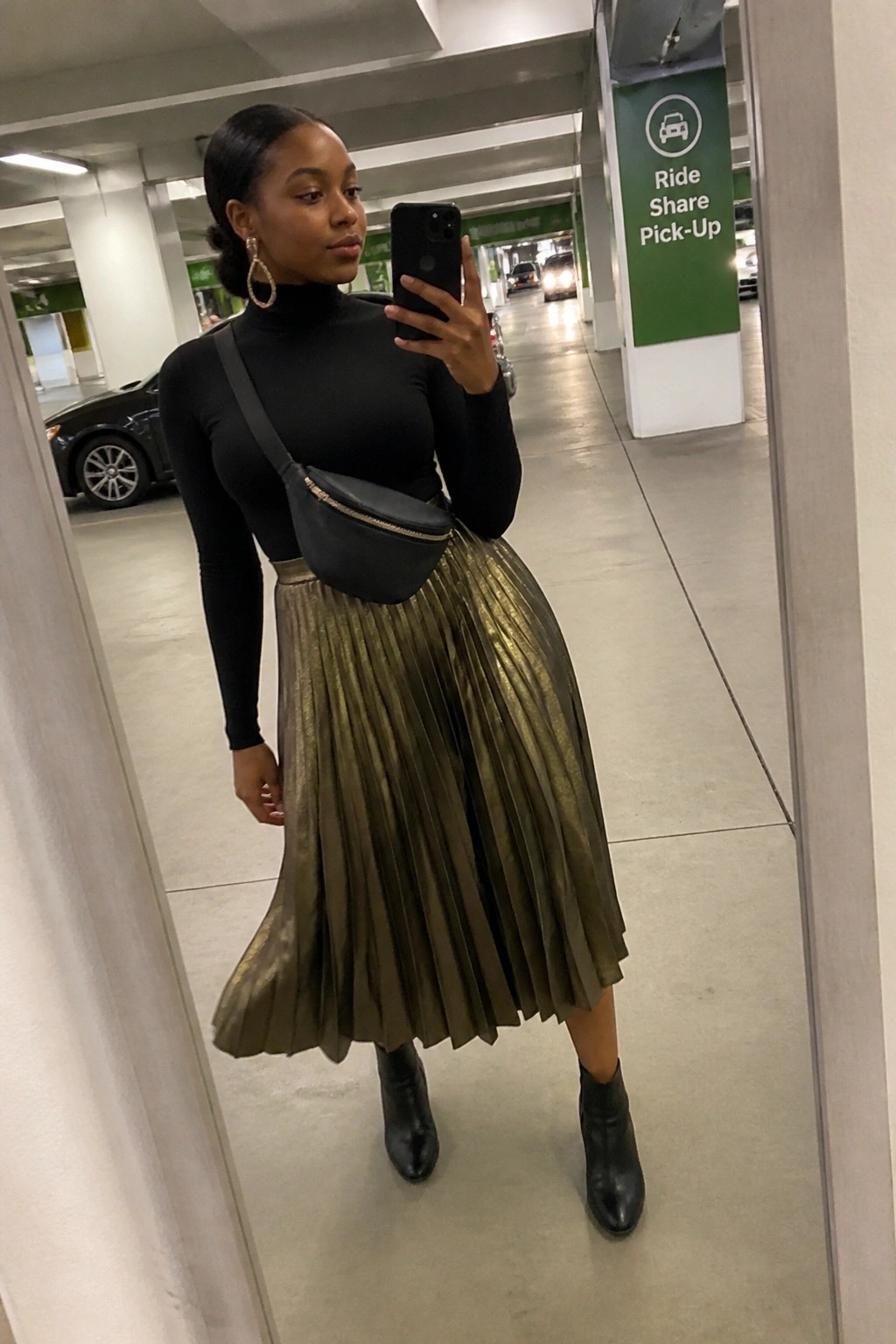 Woman in black turtleneck and metallic gold pleated skirt taking selfie in parking garage.