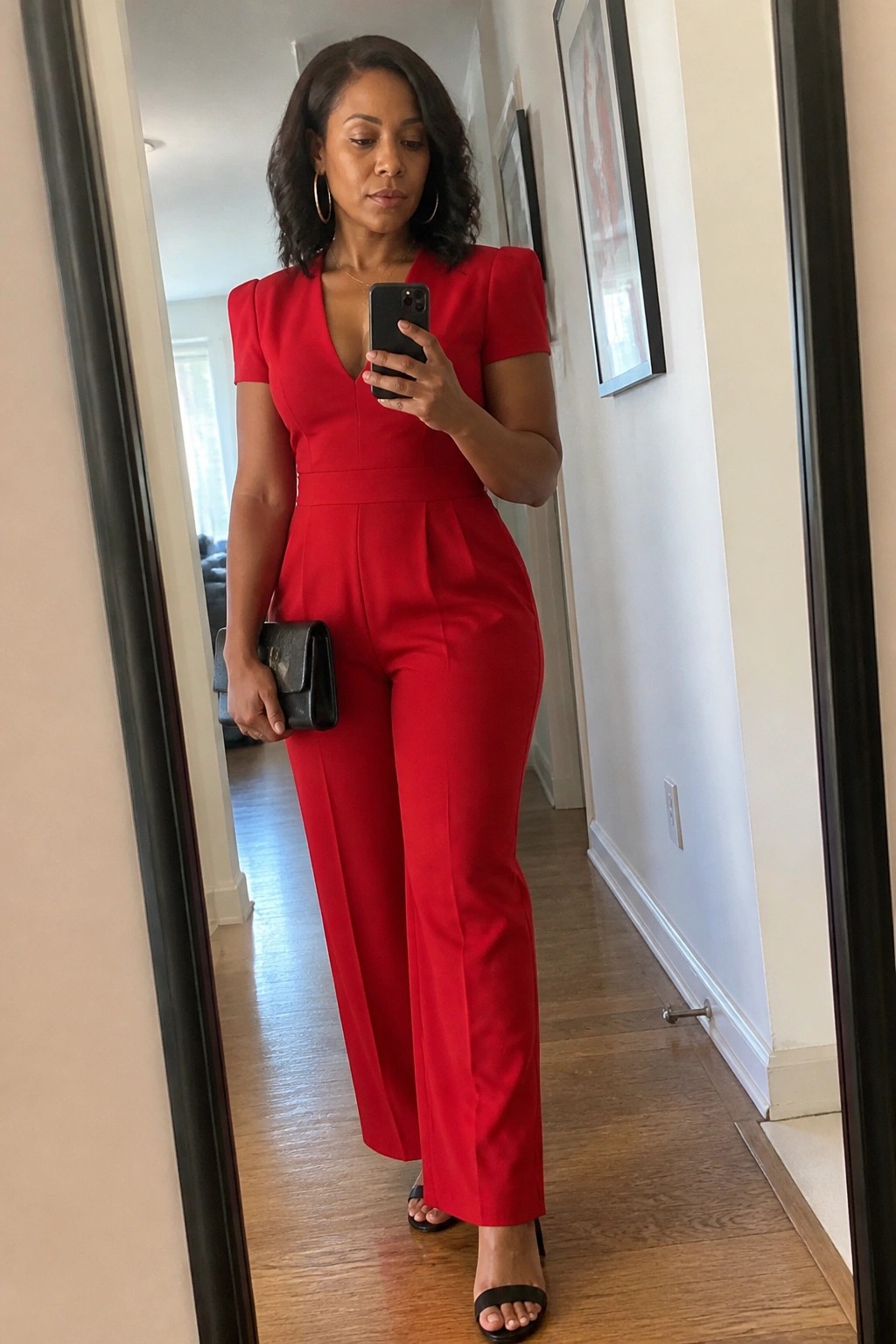 Woman in red jumpsuit taking mirror selfie while holding black clutch