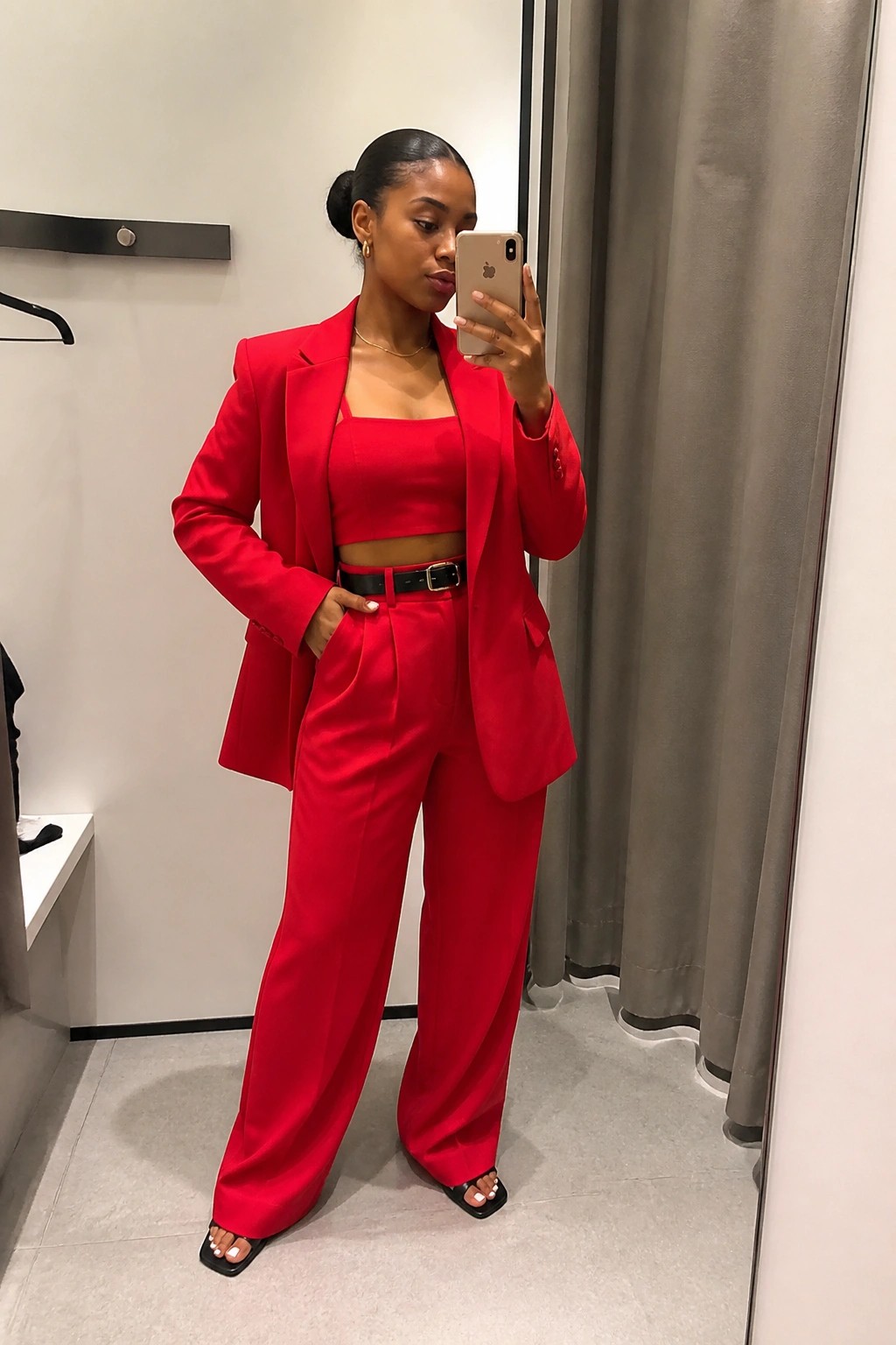 Woman in red blazer, crop top and trousers taking mirror selfie in fitting room