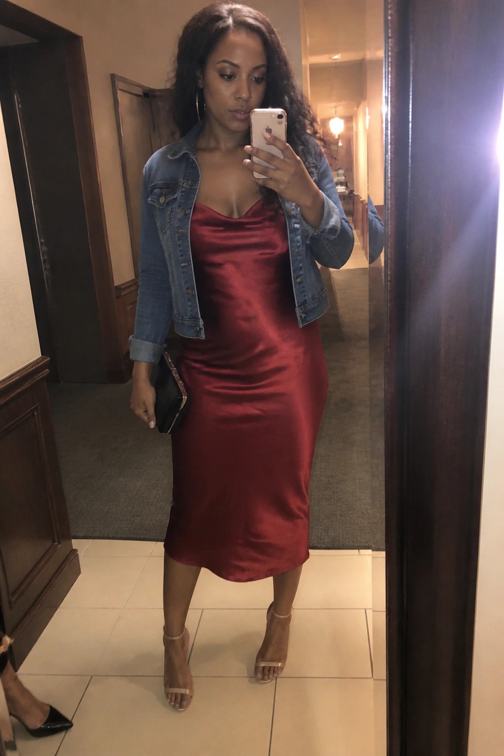 Woman in red satin dress and denim jacket taking mirror selfie with phone
