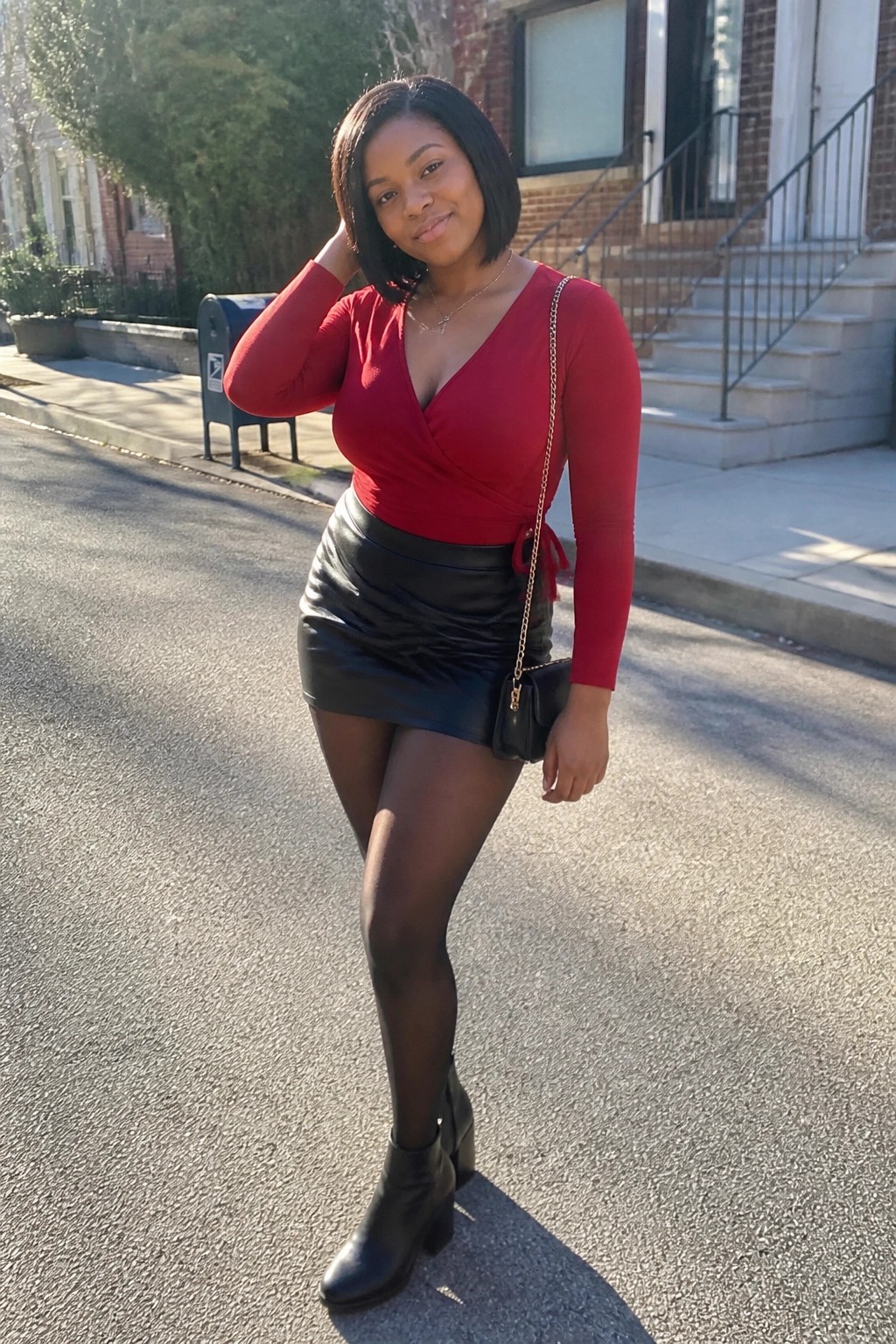 Woman in red wrap top and black leather skirt posing on sunny street