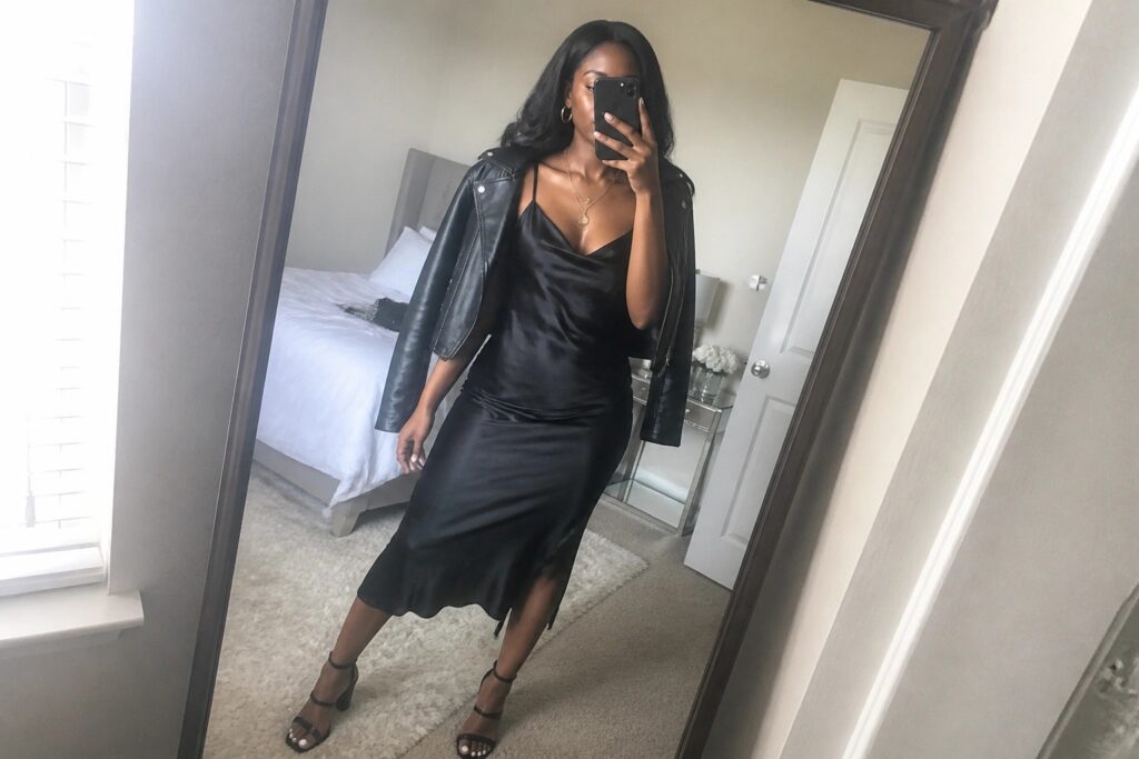 21 Chic Girls Night Out Outfit Ideas for Black Women That Stand Out After Dark Woman in black satin slip dress and leather jacket taking bedroom mirror selfie.