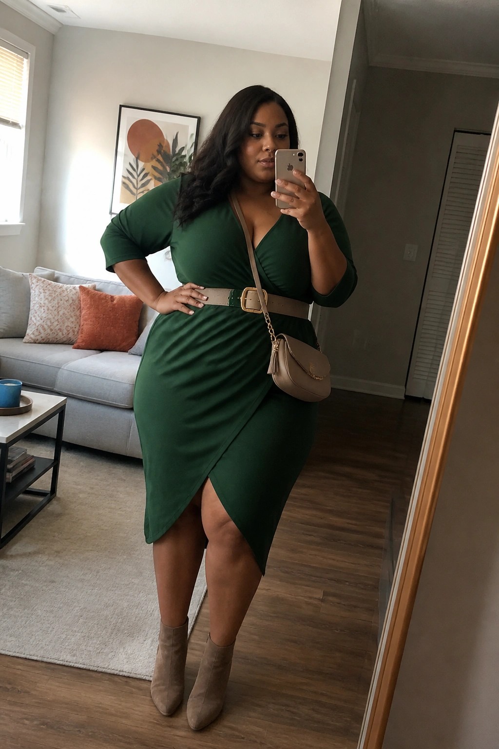 Woman in green wrap dress taking mirror selfie in modern living room with beige accessories