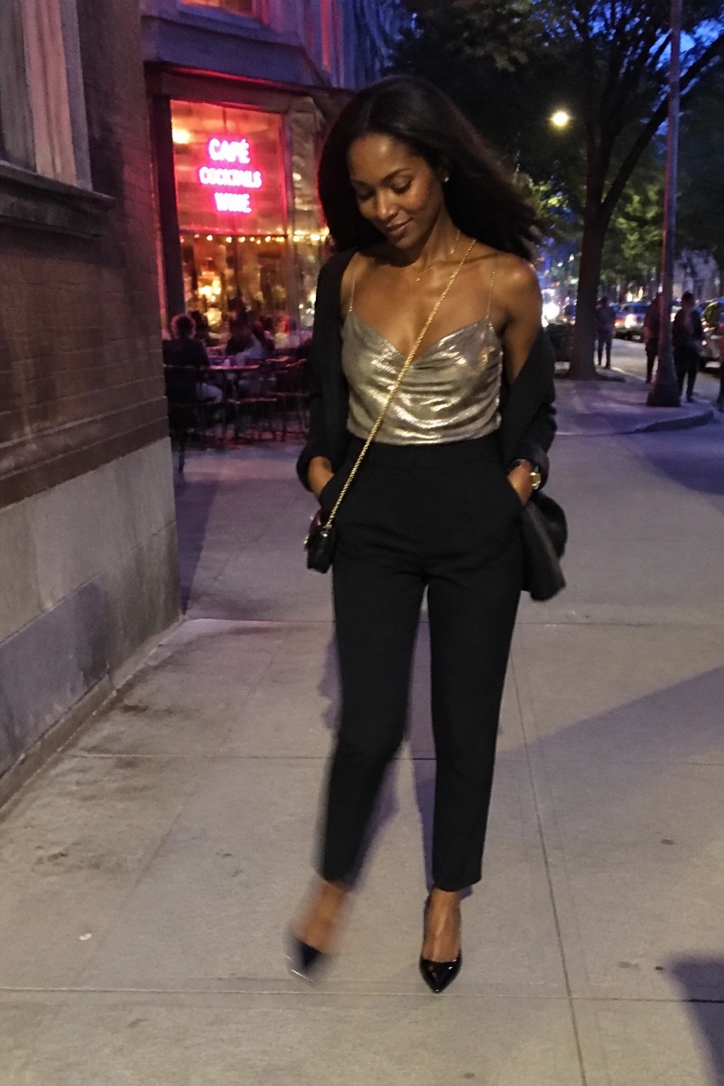 Woman in metallic gold top and black pants walking on city sidewalk at night