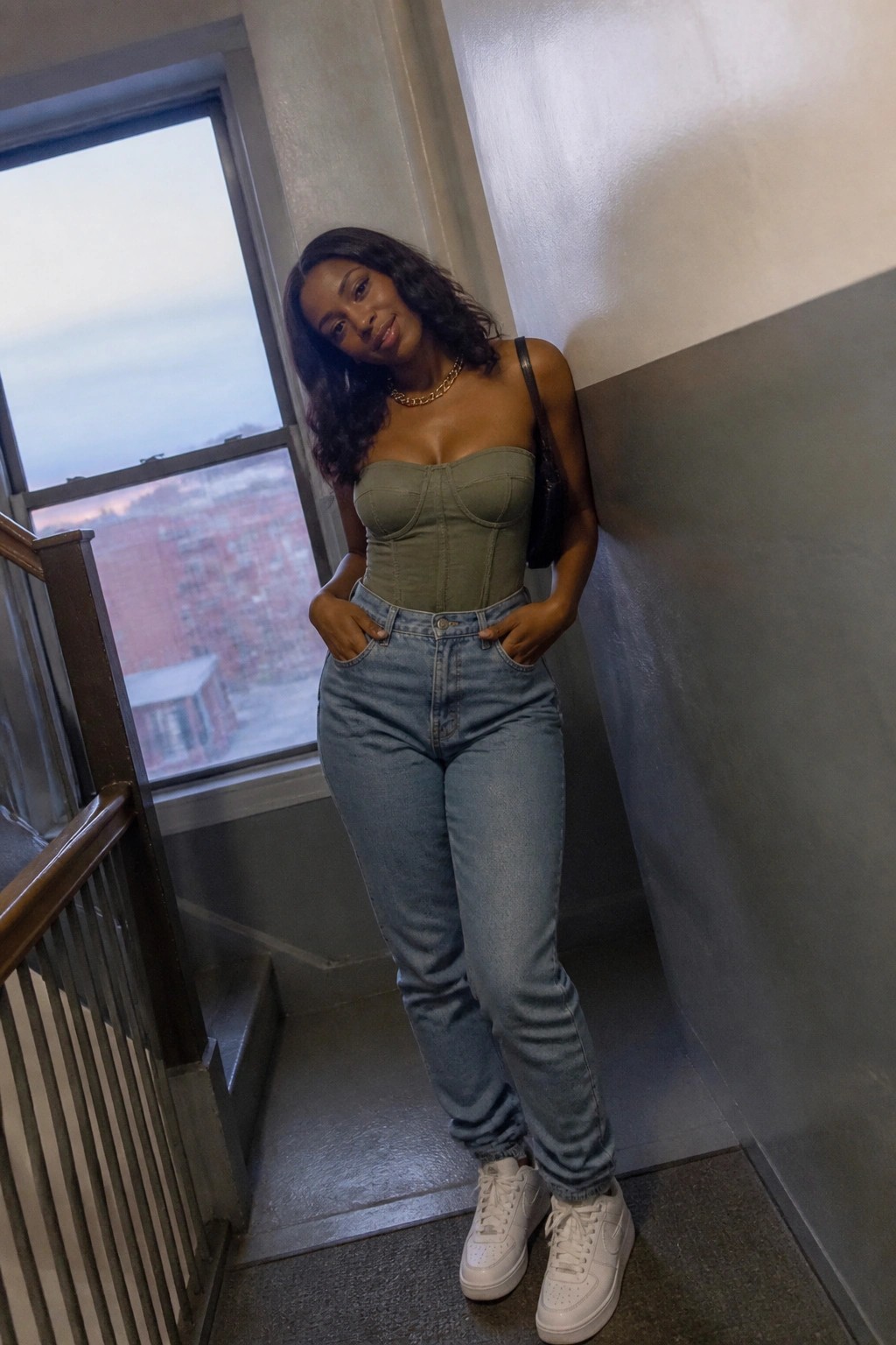 Woman in sage green corset top and blue jeans posing in stairwell