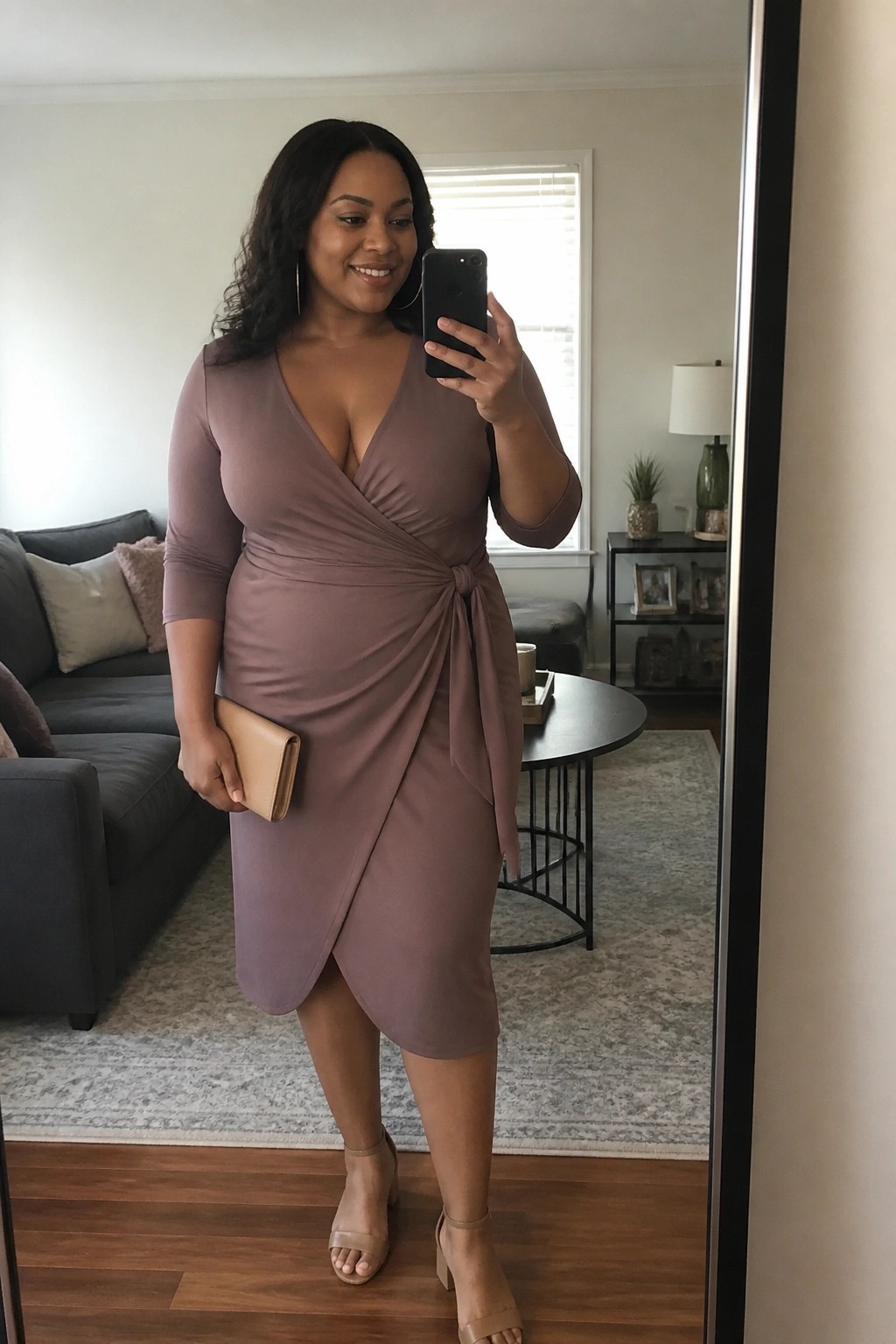 Woman in mauve wrap dress taking mirror selfie in living room