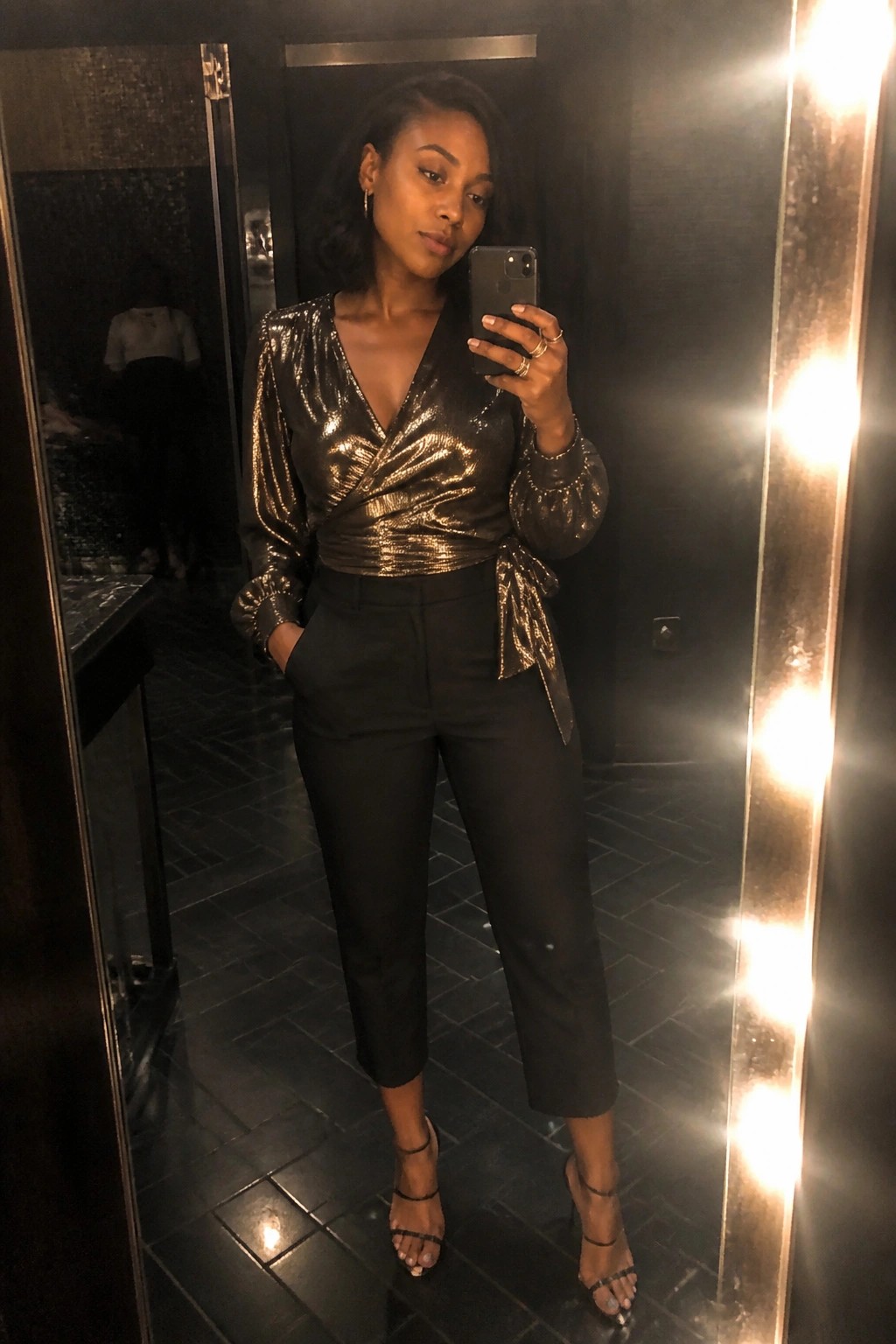 Woman in gold sequined wrap top and black pants taking mirror selfie