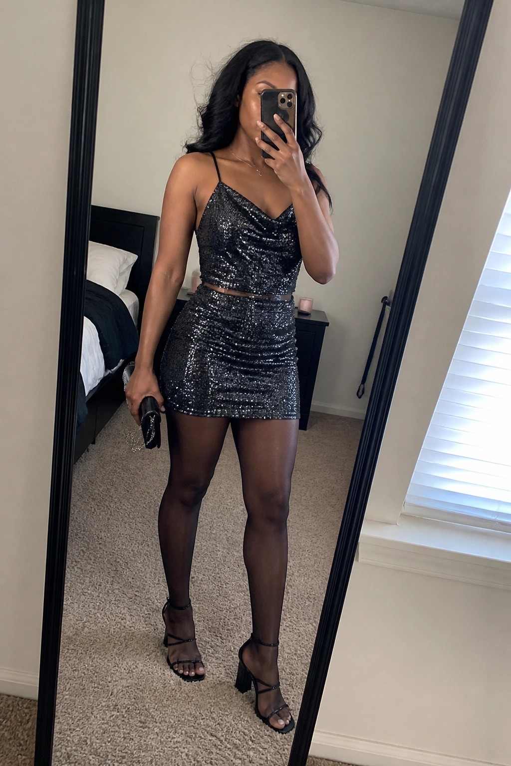 Woman in black sequined crop top and mini skirt taking bedroom mirror selfie.