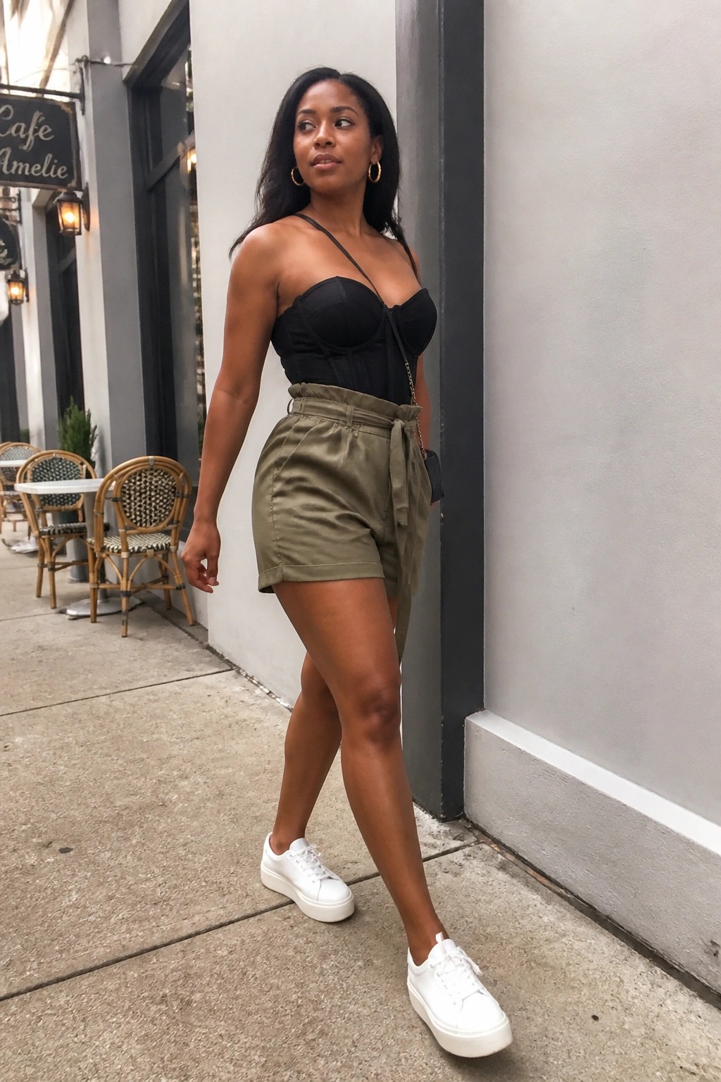Woman in black corset top and olive shorts with white sneakers on sidewalk