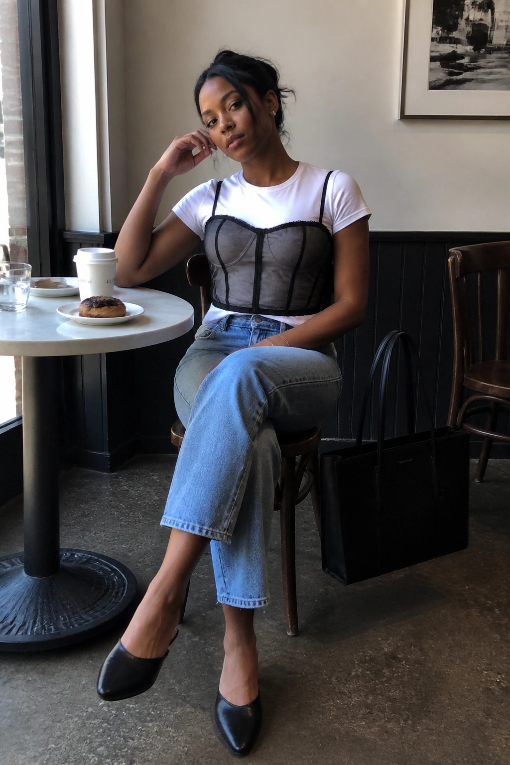 Woman in sheer grey corset over white tee and blue jeans at cafe table