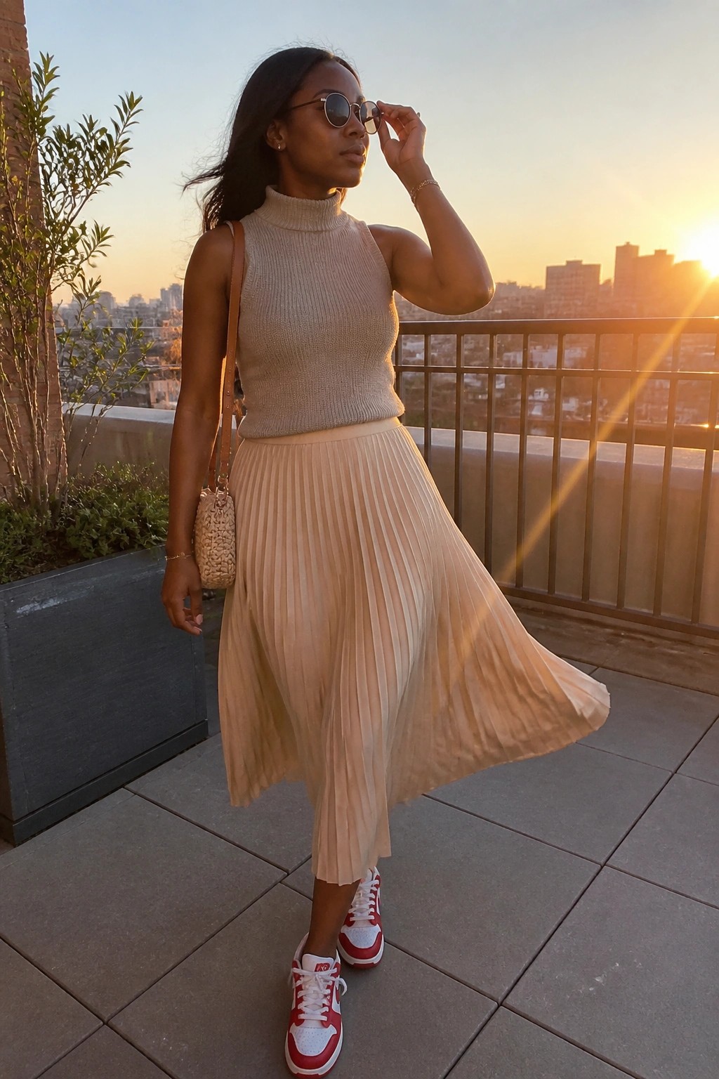 Woman in beige turtleneck and pleated skirt adjusting sunglasses on sunset balcony