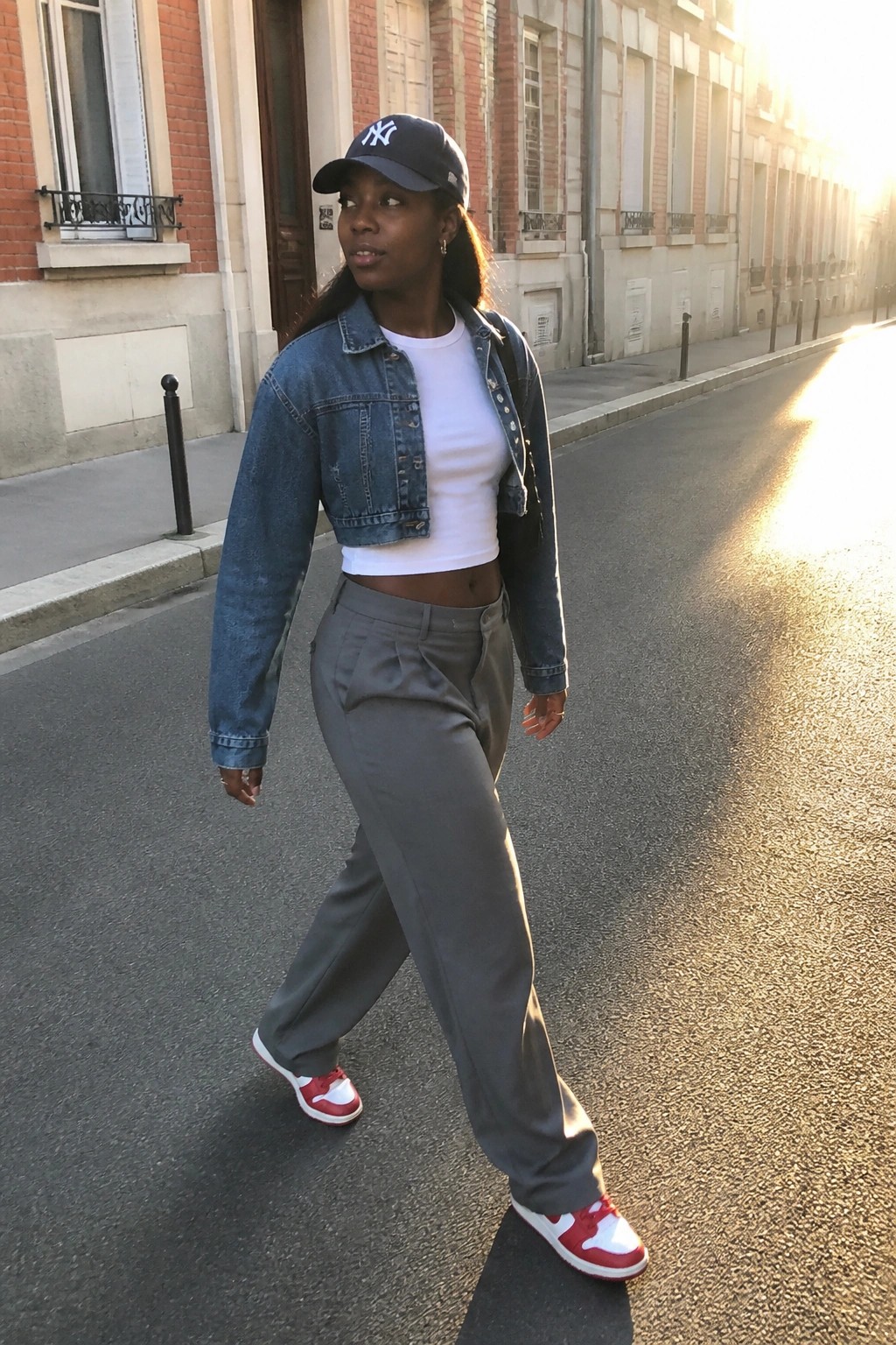 Young woman in cropped denim jacket and NY cap walks on sunny street