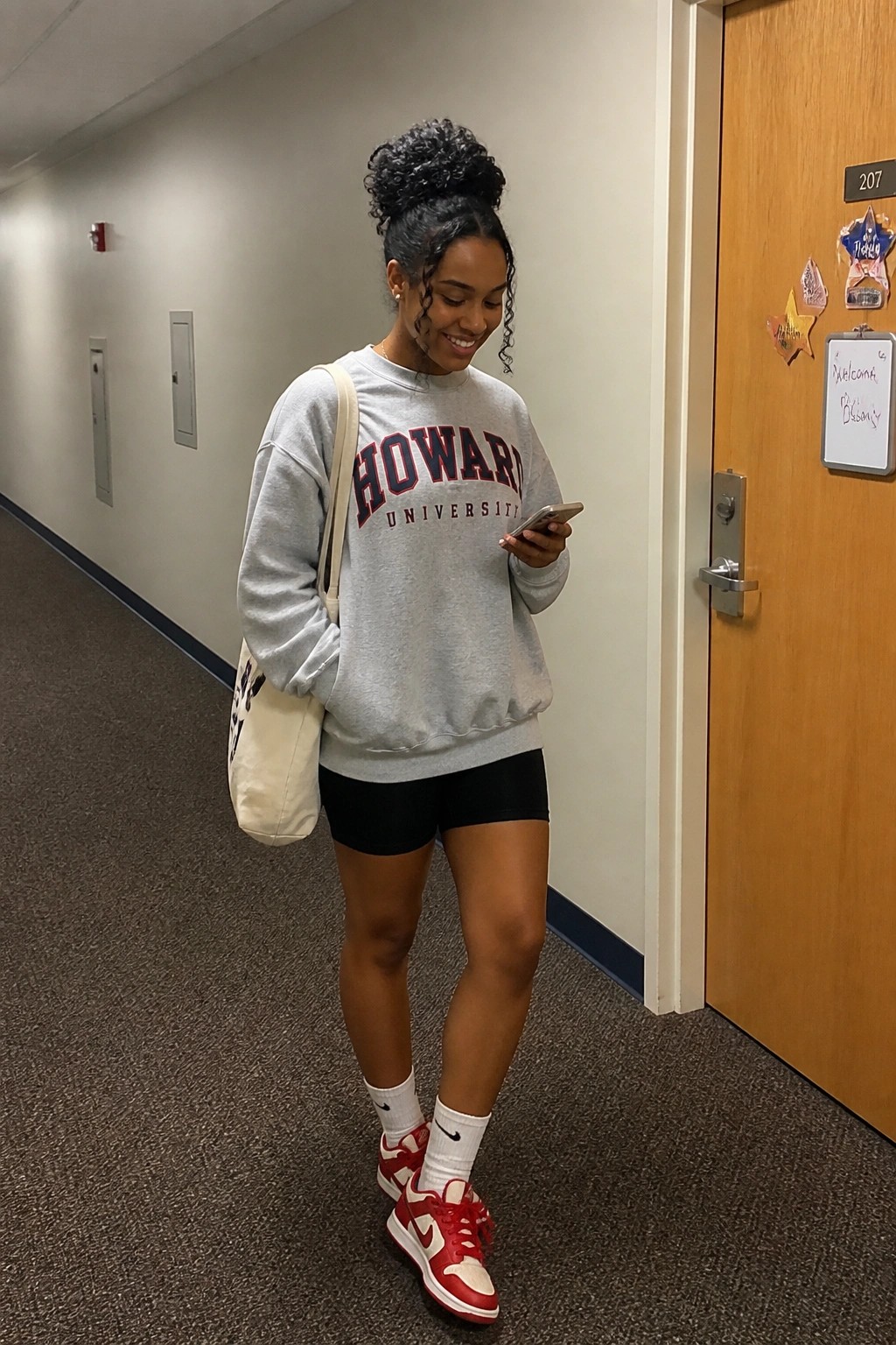 Woman in gray Howard University sweatshirt and red Nike sneakers checks phone in hallway