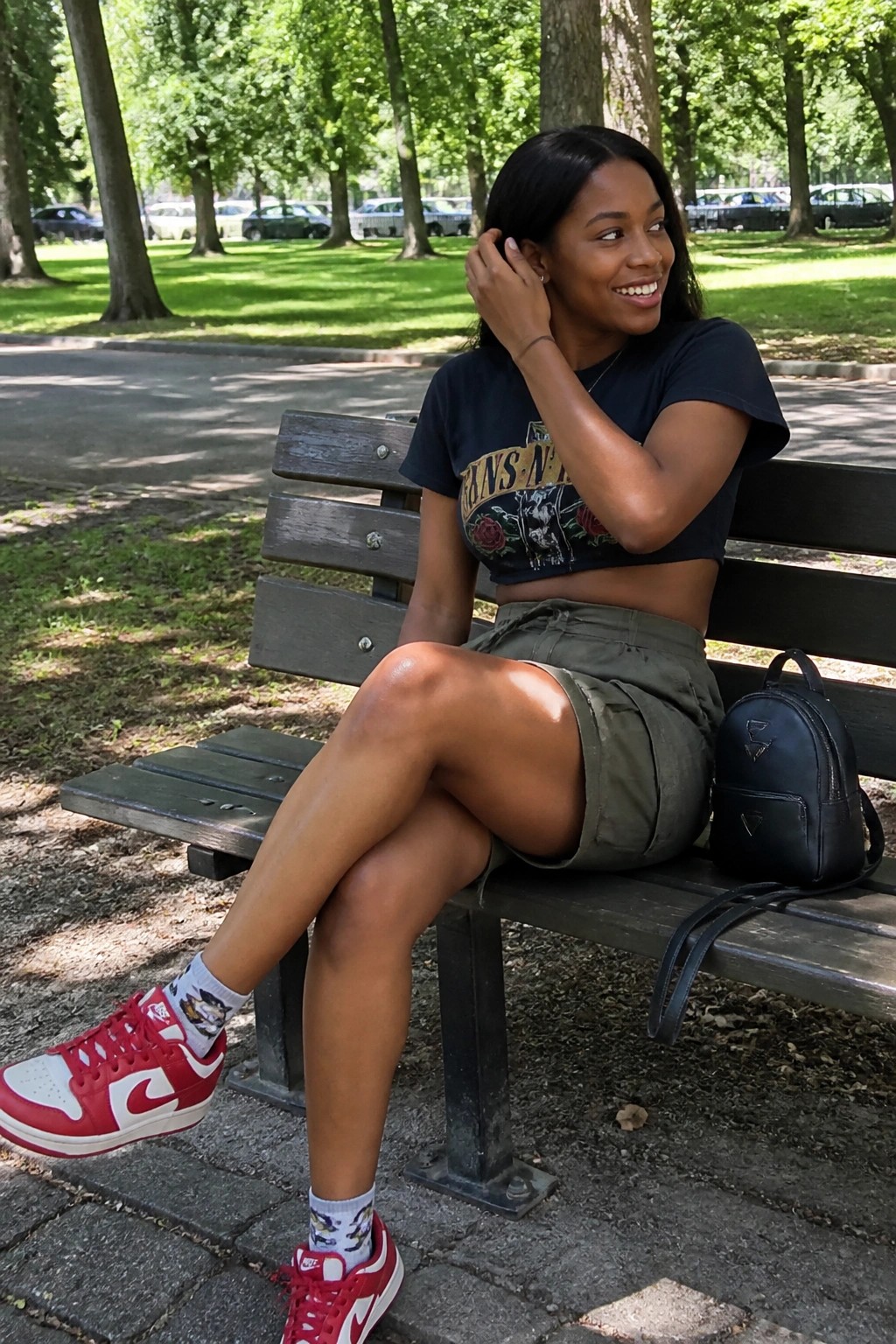Smiling woman in black crop top and olive shorts on park bench with red sneakers