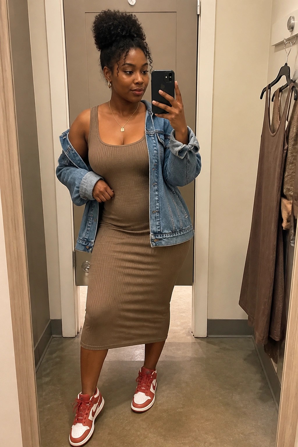 Woman in brown ribbed dress and denim jacket taking mirror selfie in red sneakers