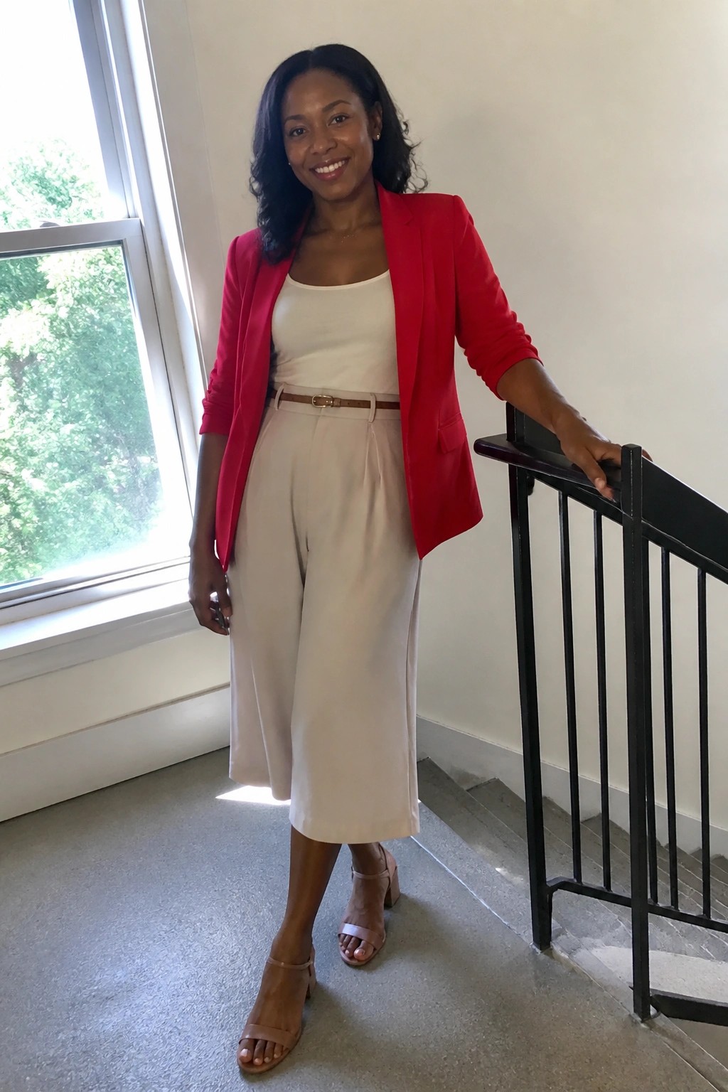 Woman in red blazer and beige pants leaning on black stair railing