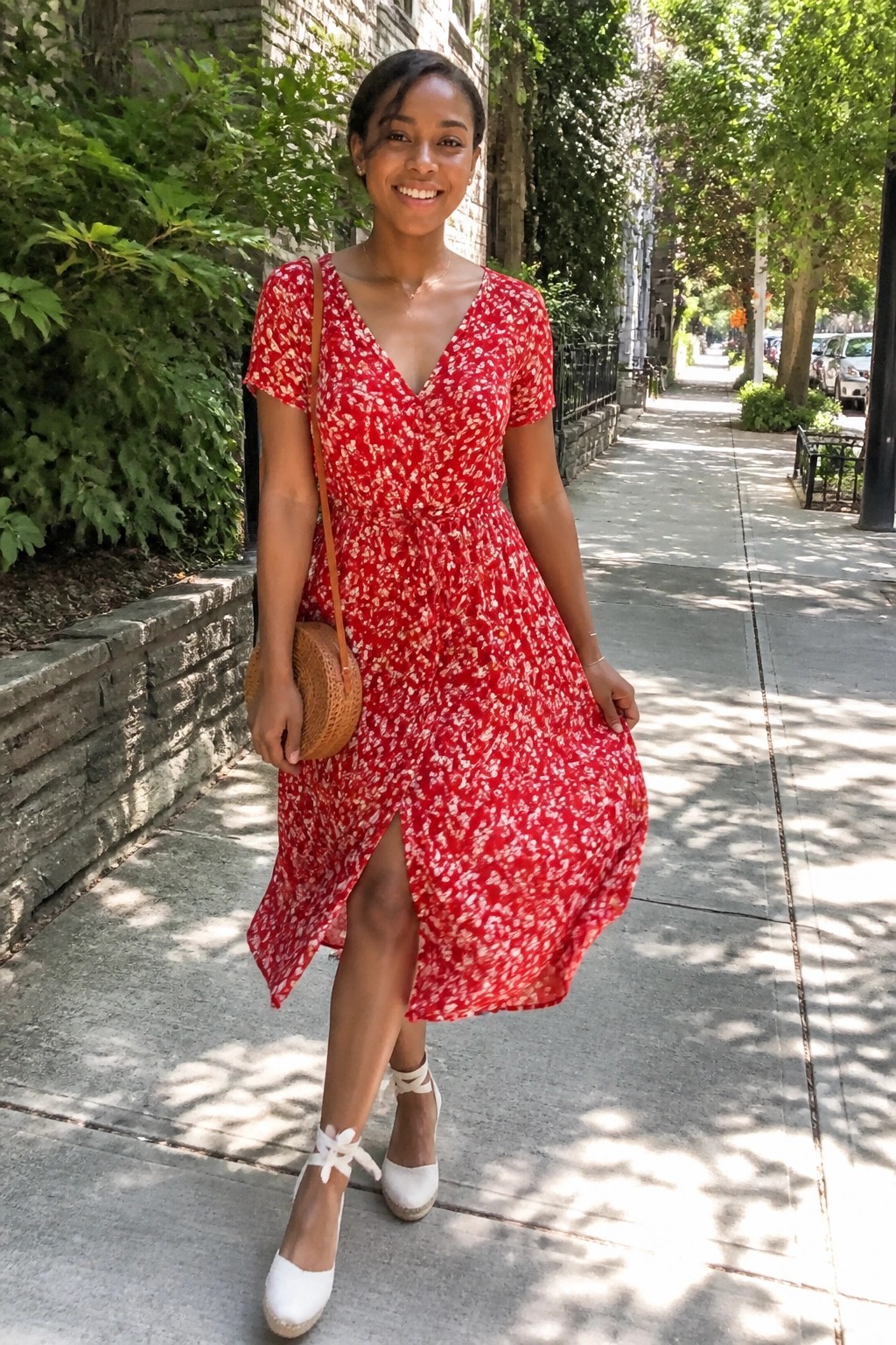 Woman in red floral dress with wicker bag on sunny sidewalk