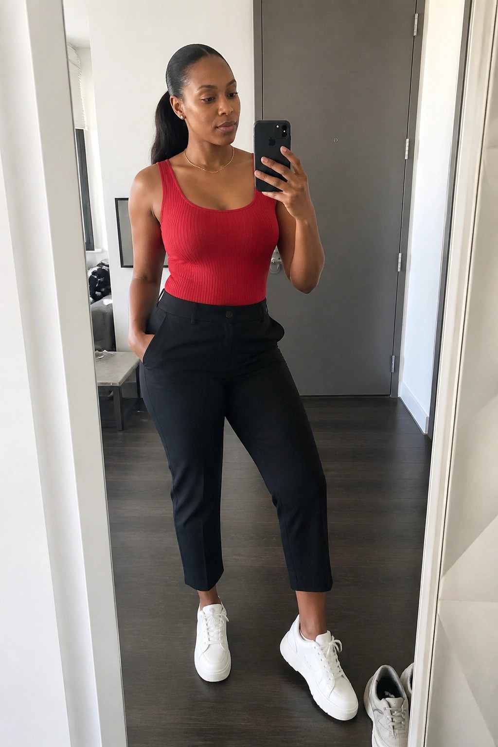 Woman in red ribbed top and black pants taking mirror selfie in white sneakers