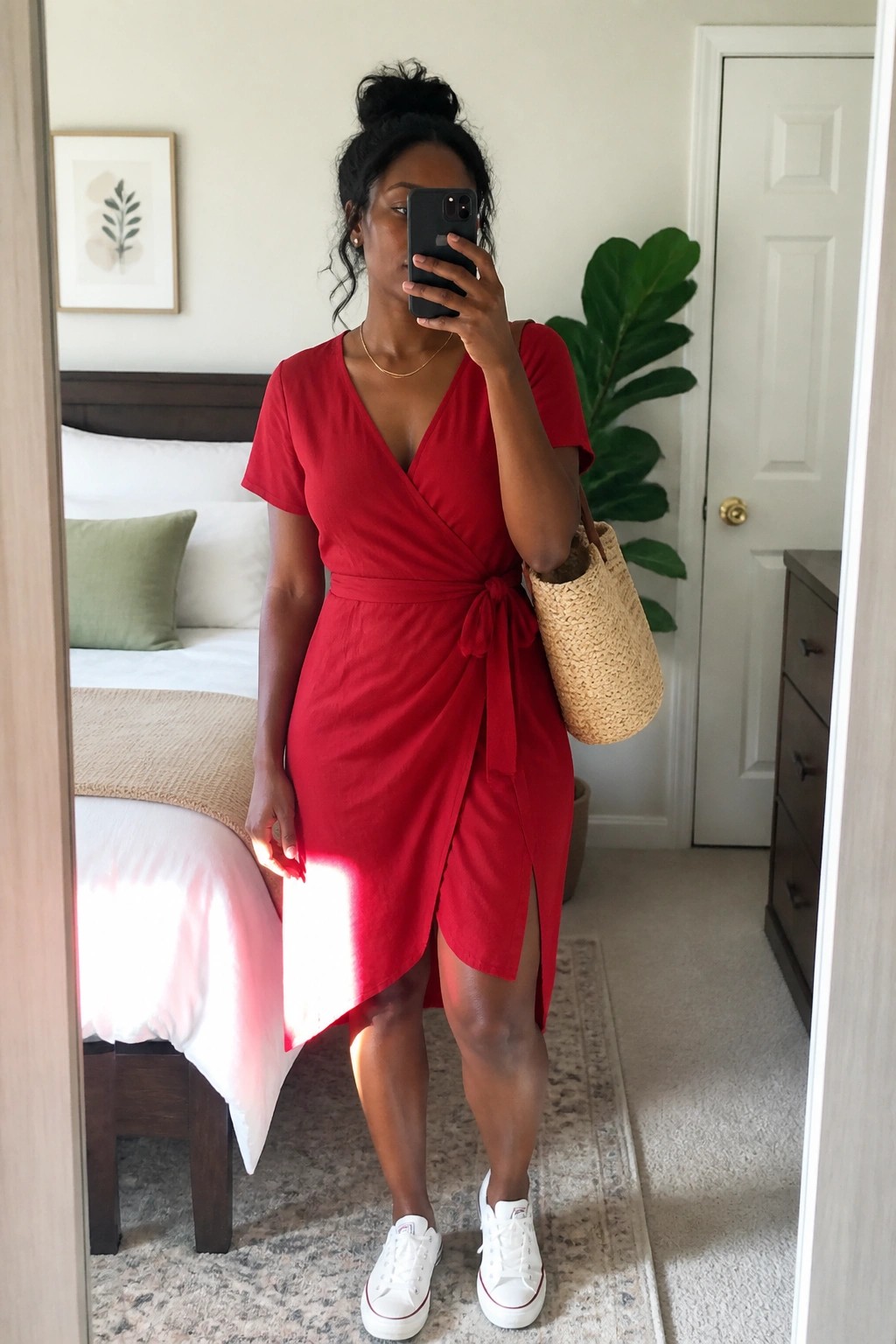 Woman in red wrap dress taking mirror selfie with straw bag and white sneakers
