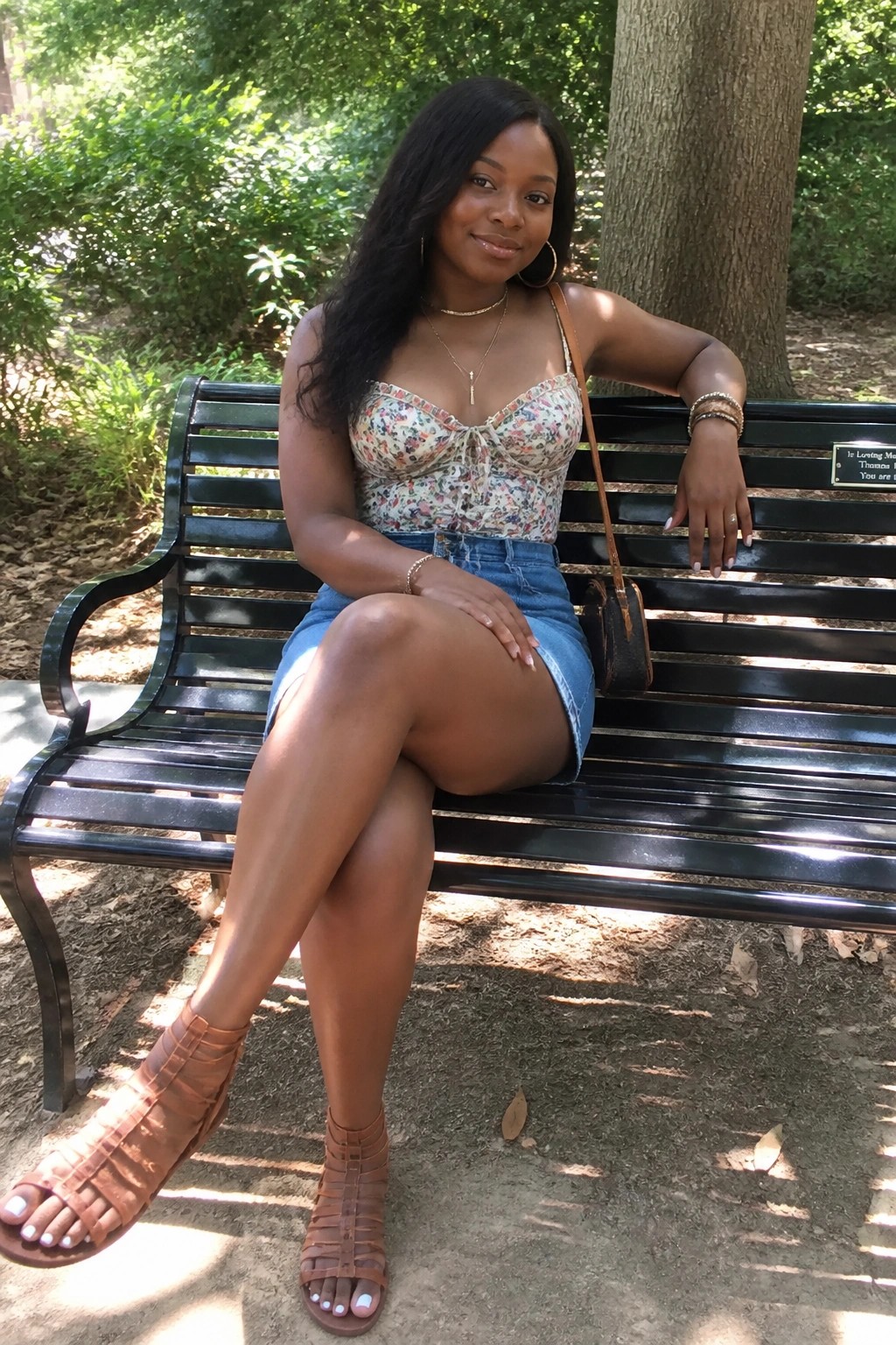 Woman in floral top and denim skirt seated on black park bench