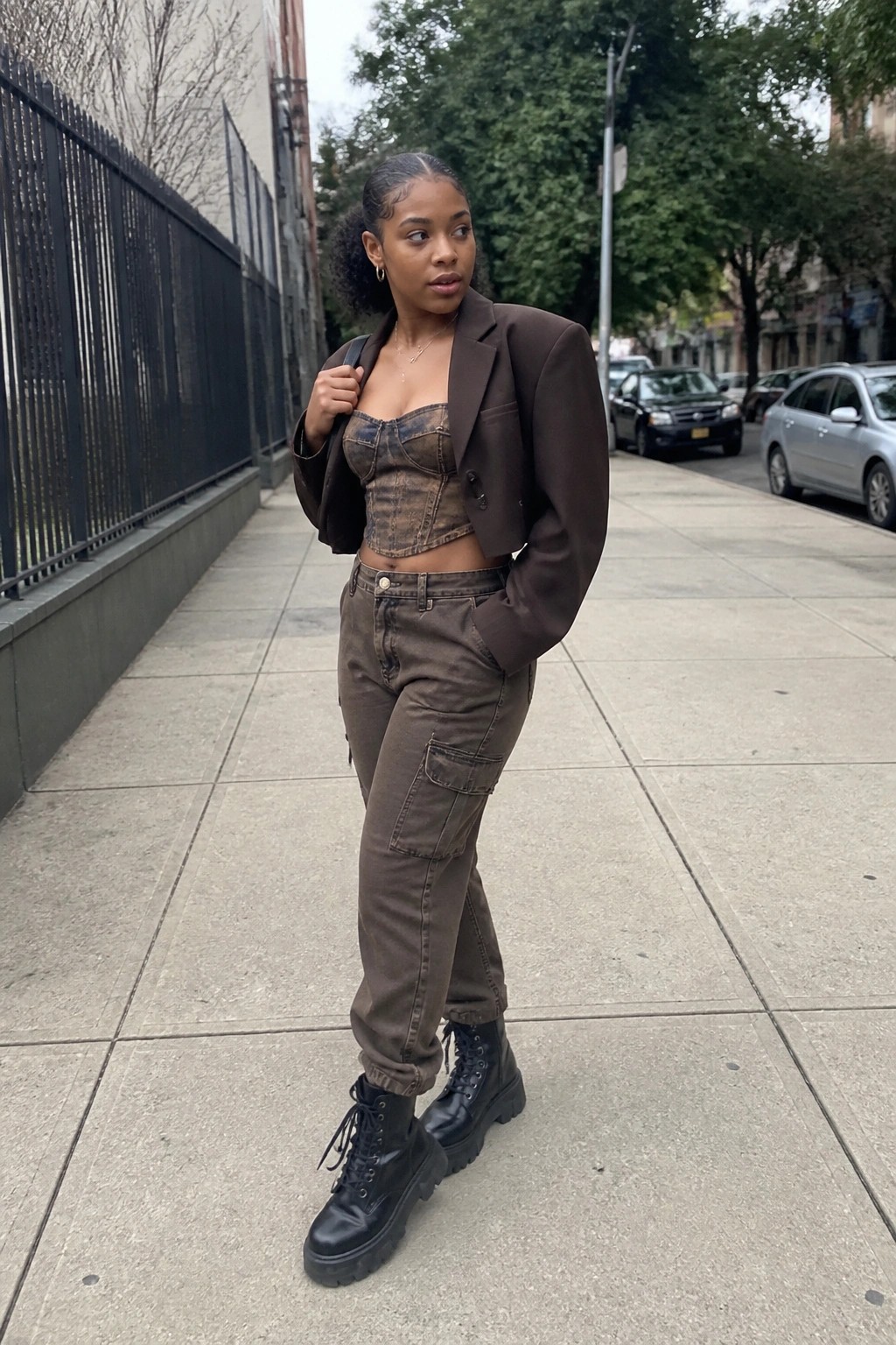 Woman in brown cropped blazer, denim corset, cargo pants, and black boots on sidewalk